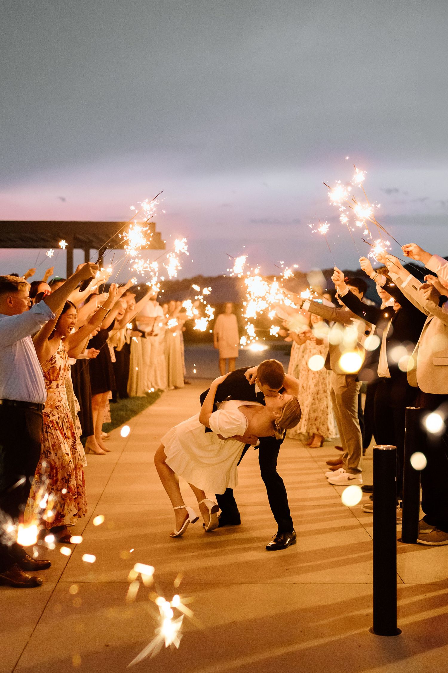 Wedding guests form two lines holding sparklers in the dark as a newlywed couple makes their grand exit celebration.