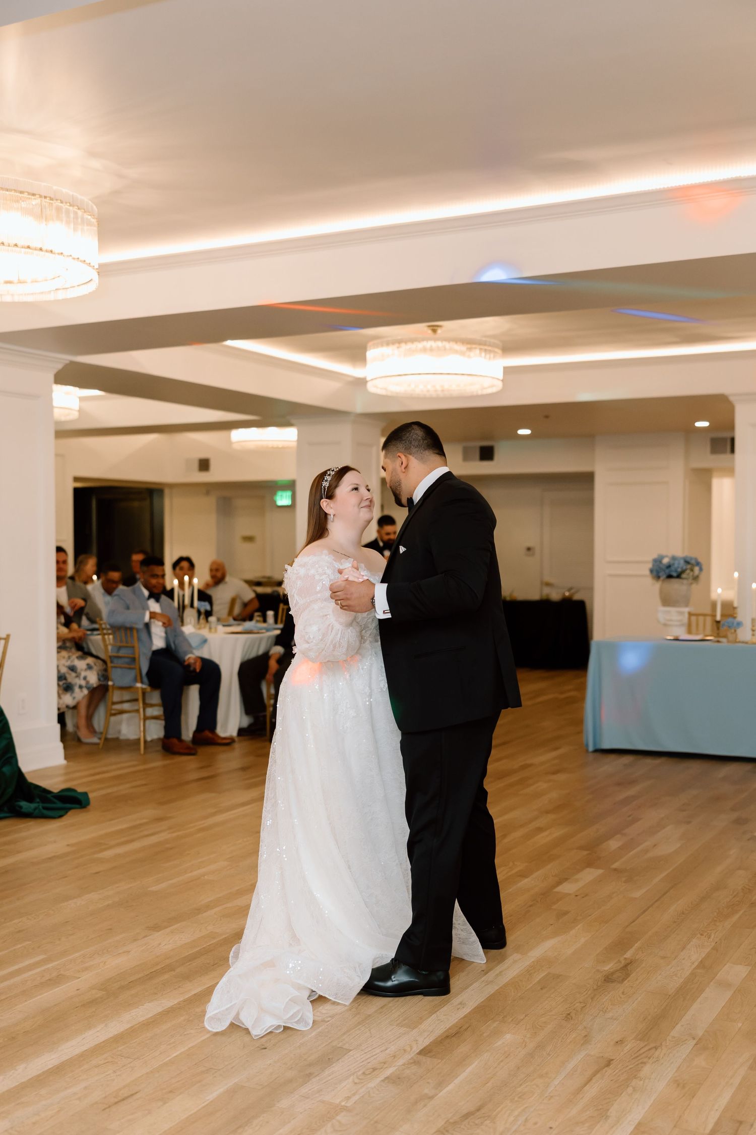 Bride and groom share their first dance on a wooden floor at an elegant wedding reception venue.