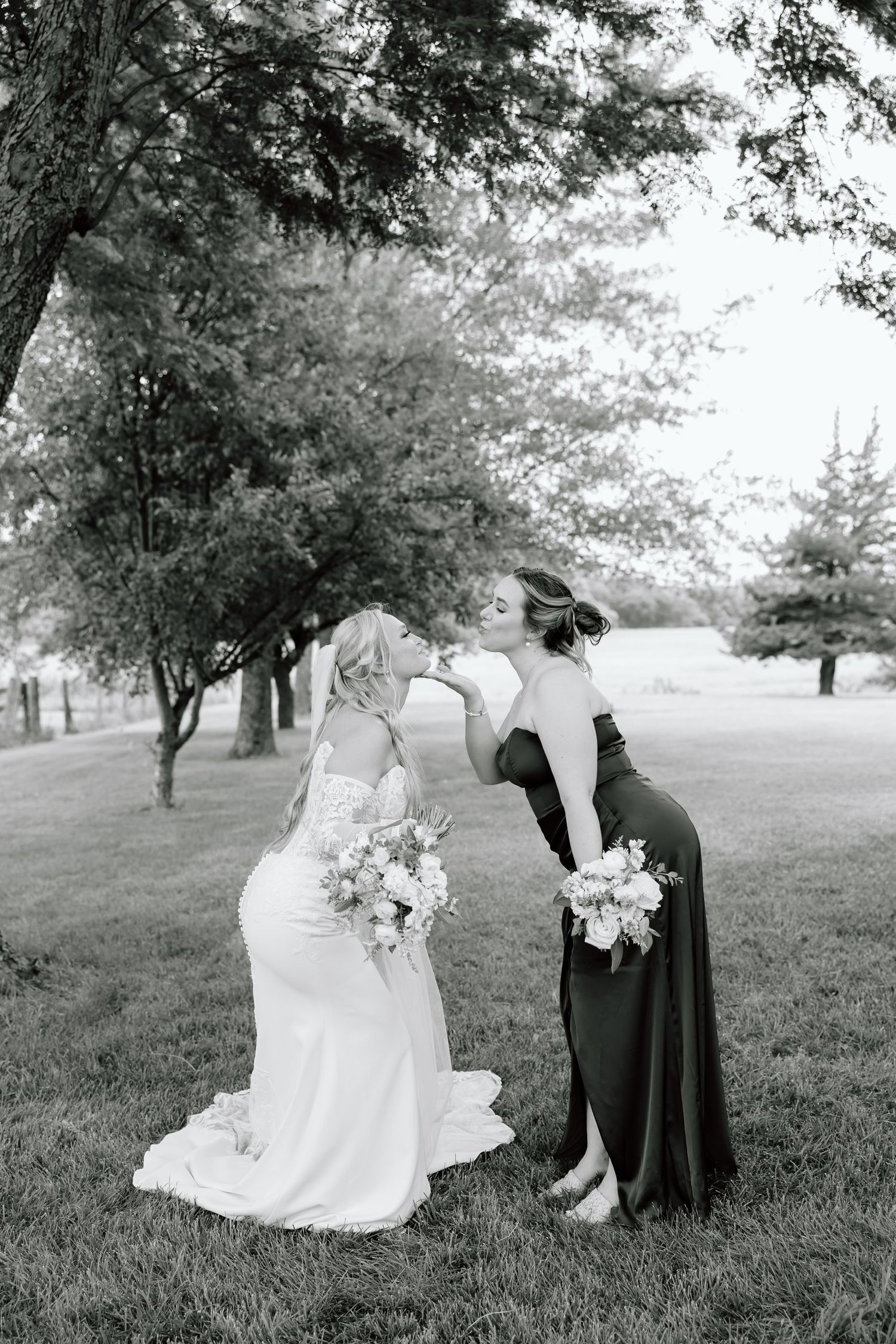 Bride and bridesmaid share a tender moment holding bouquets outdoors in a black and white wedding photo.