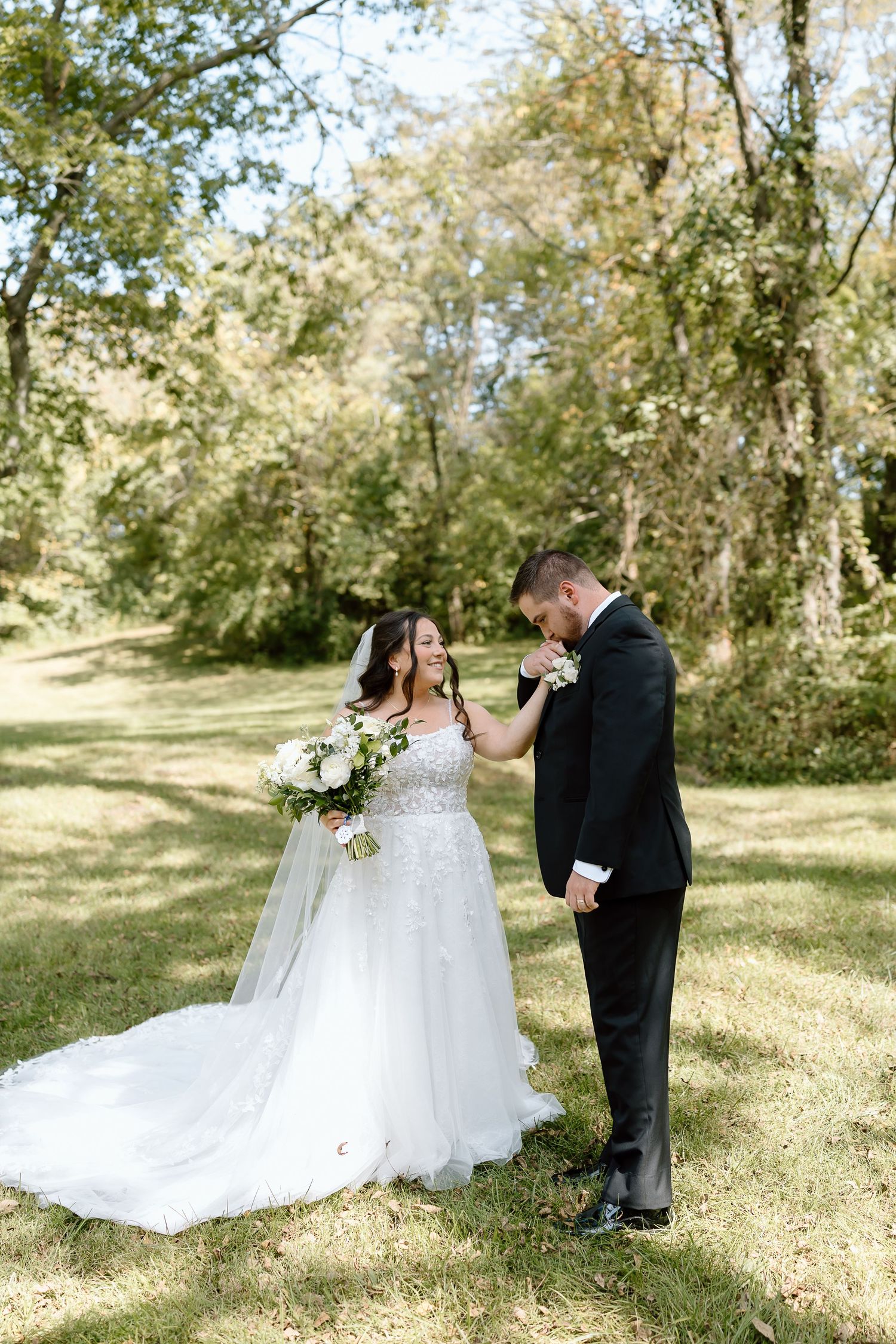 A romantic first look moment between newlyweds in a sun-dappled outdoor setting with flowing white dress details.