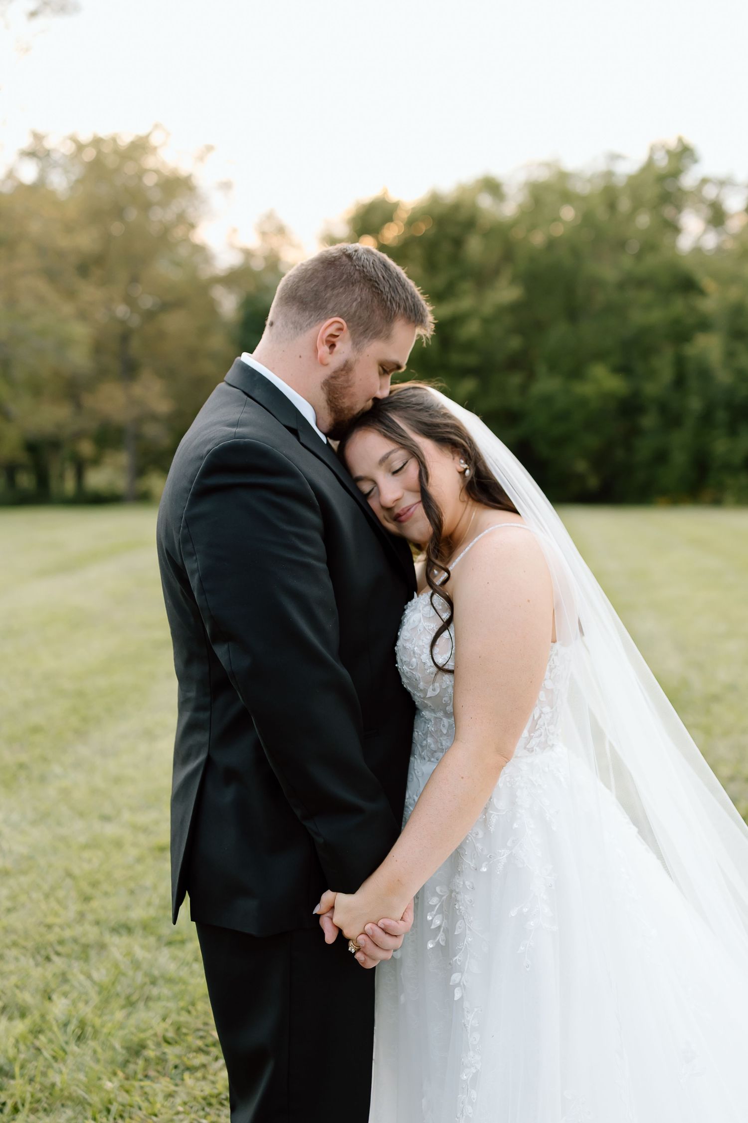 Newlywed couple shares intimate moments in a serene outdoor setting with golden sunlight and green fields.