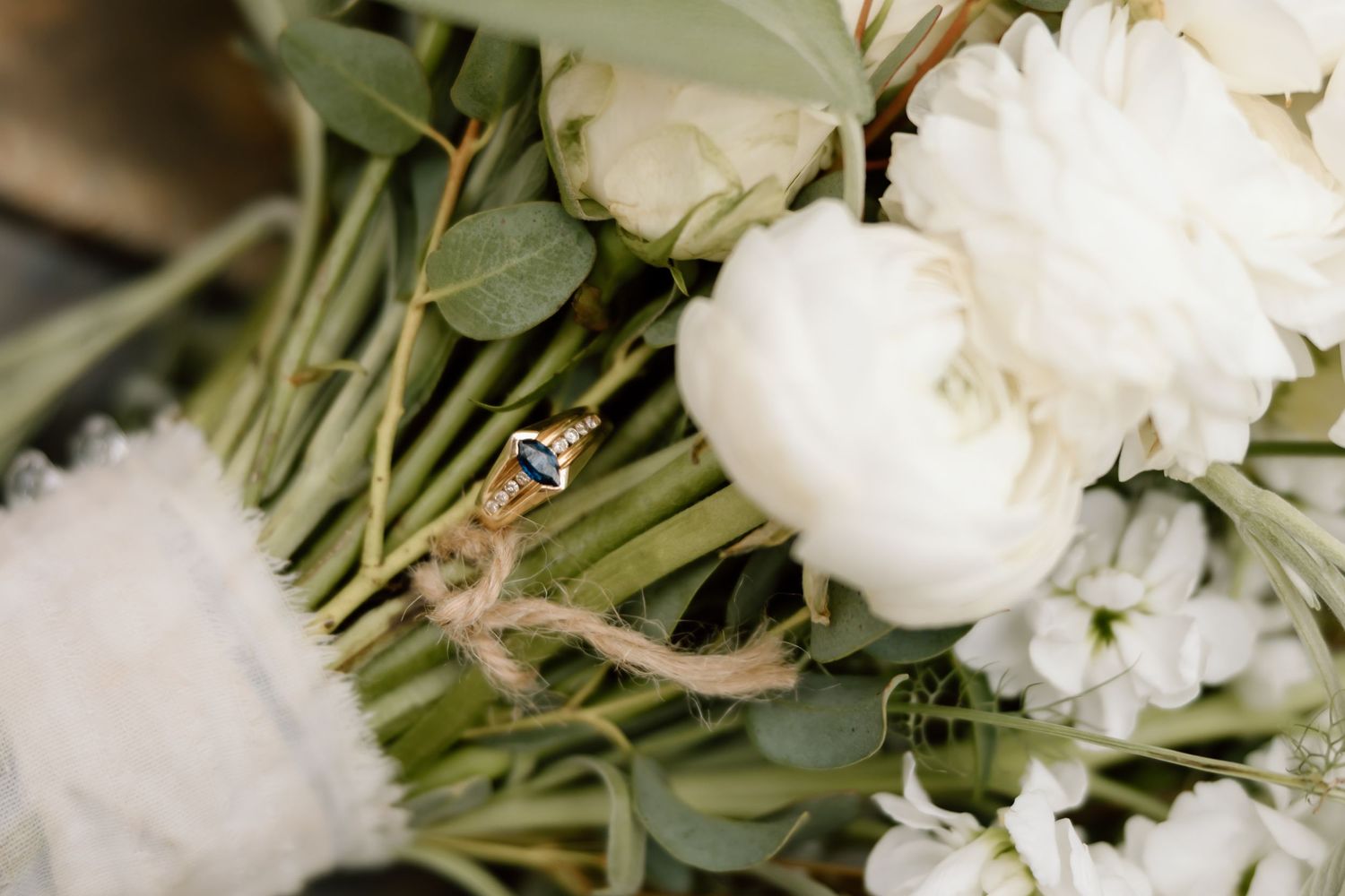 Wedding rings nestled in a bridal bouquet of white peonies and eucalyptus greenery tied with twine.