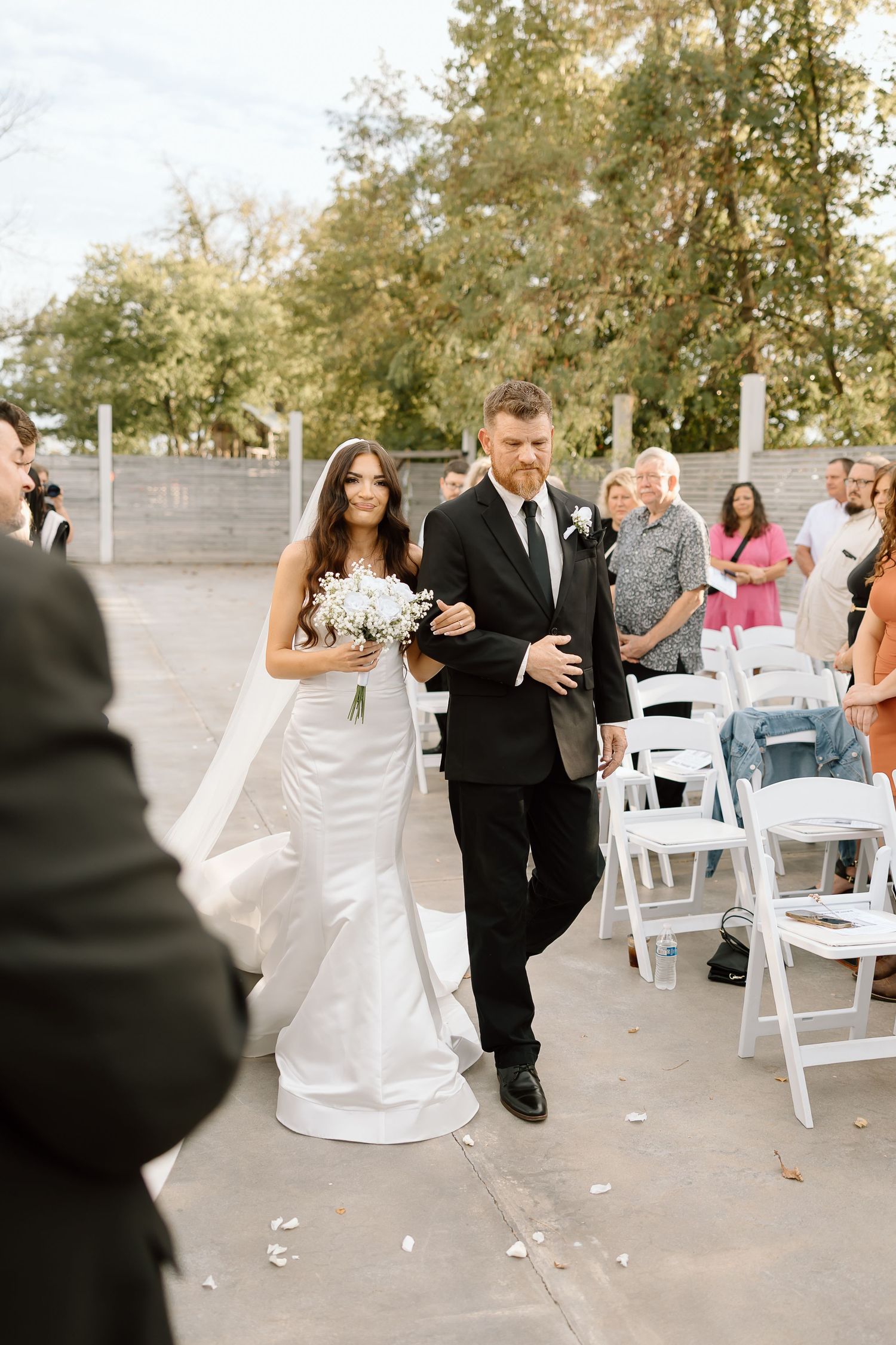 A couple shares a romantic dance together at an outdoor wedding reception surrounded by white chairs and guests.