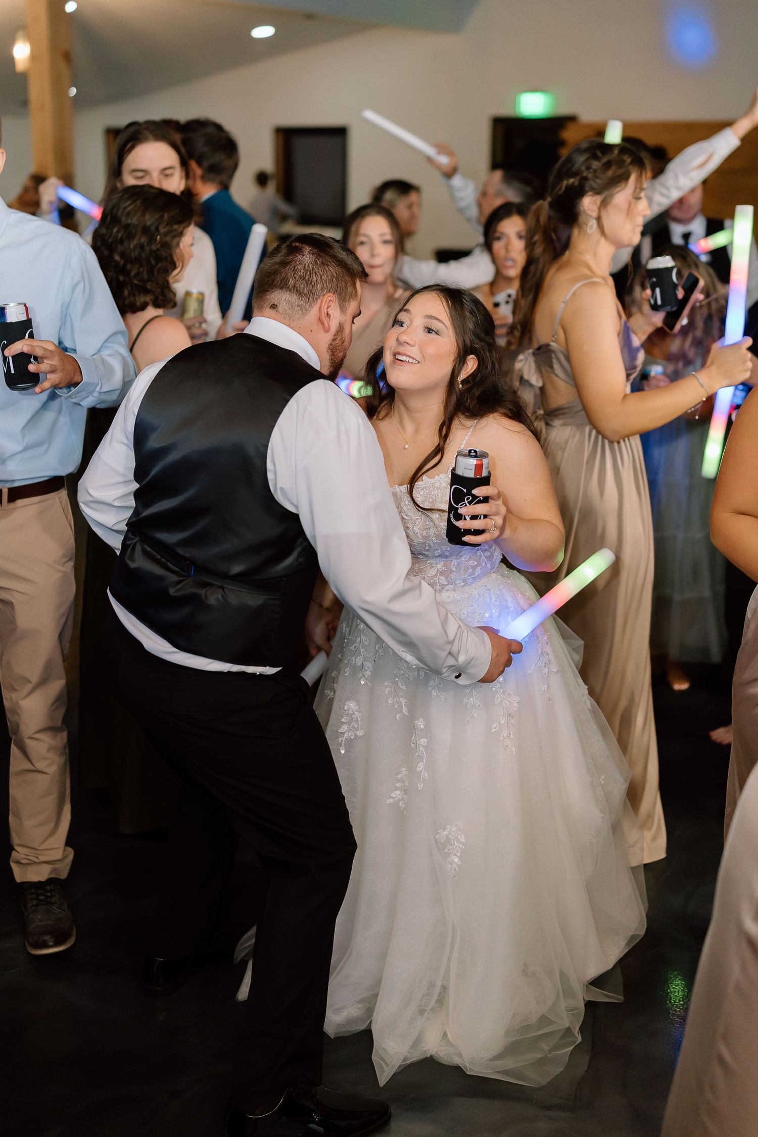 Wedding guests dance and celebrate on a dimly lit dance floor at an indoor reception venue.