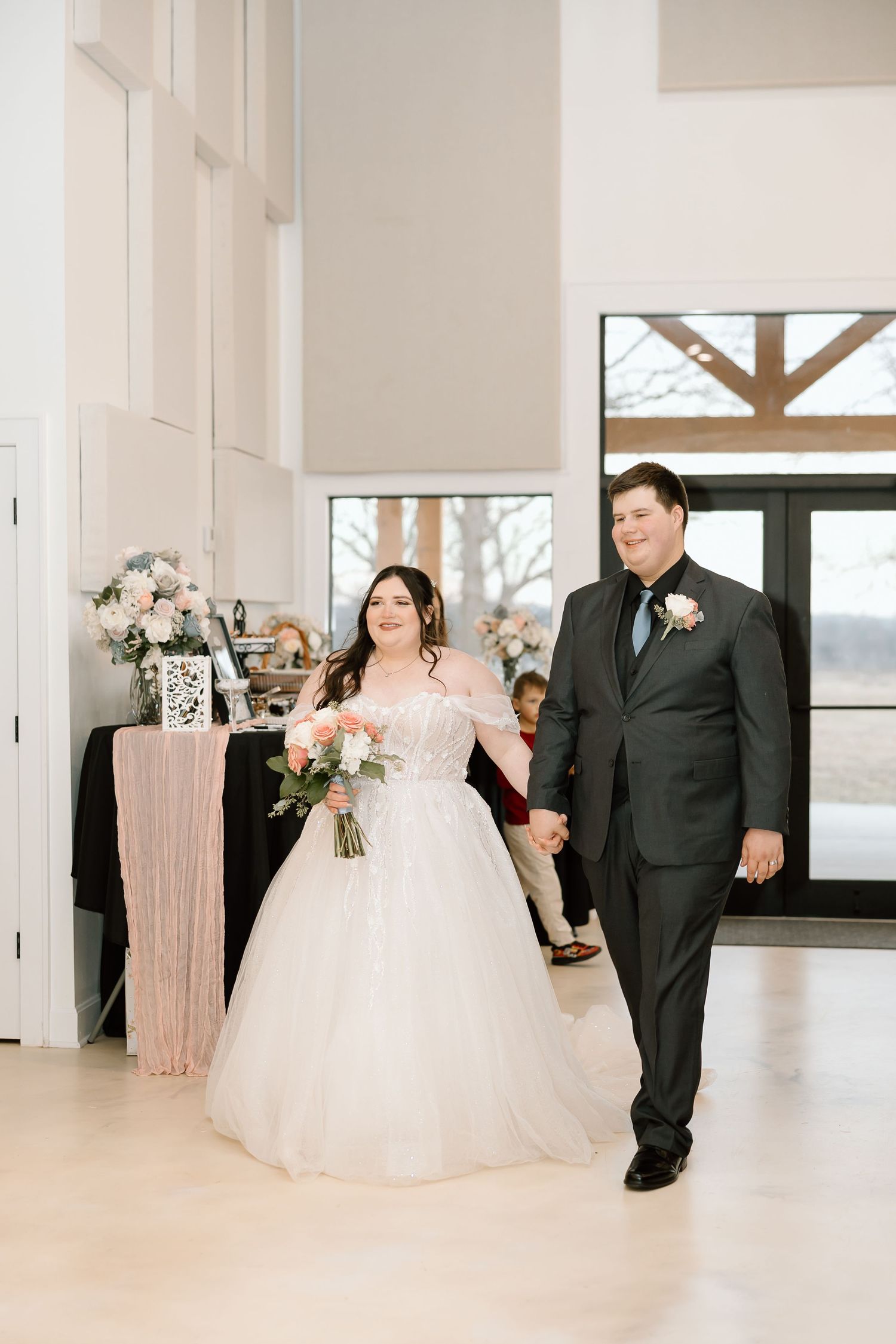 Bride and father share emotional first look moment in bright white modern venue with large windows.