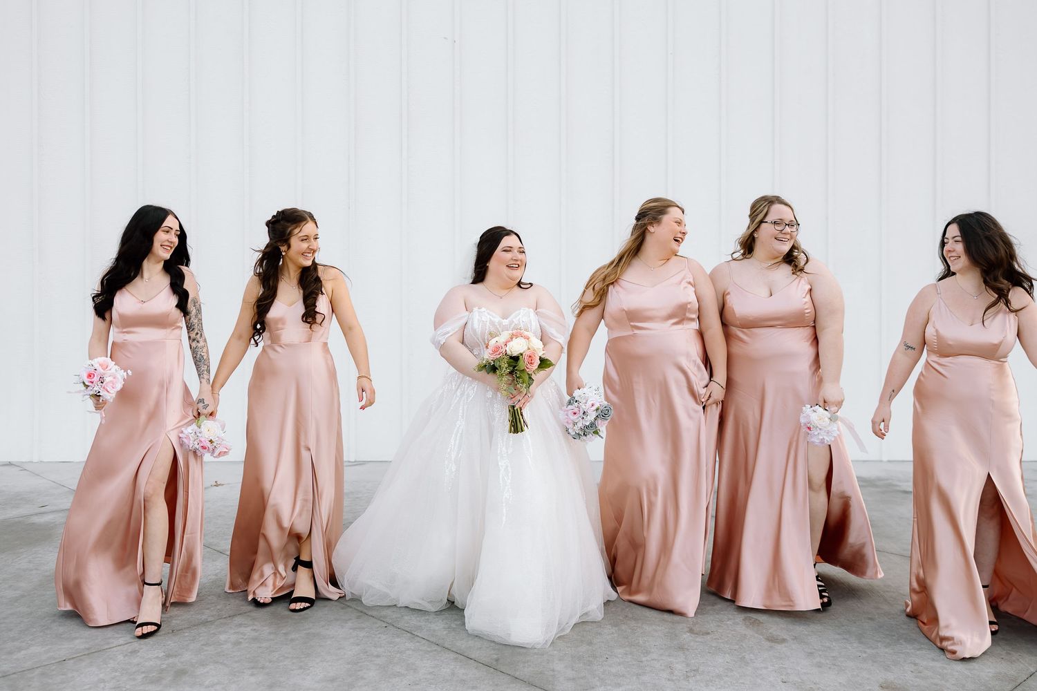 Bridesmaids in blush pink dresses pose with bride in white gown during wedding photoshoot.