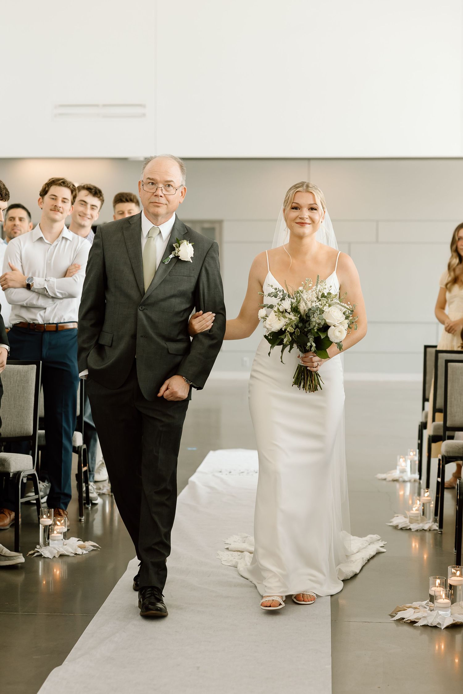 Sequence of wedding ceremony shots showing a bride walking down a minimalist indoor aisle with candlelight.