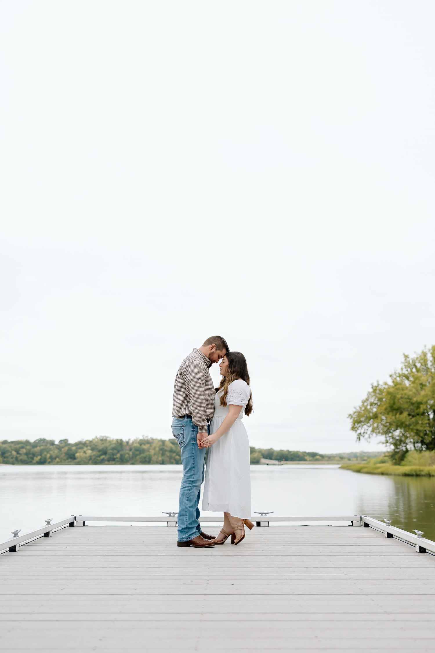 A couple in casual attire shares a romantic moment on a lakeside dock.