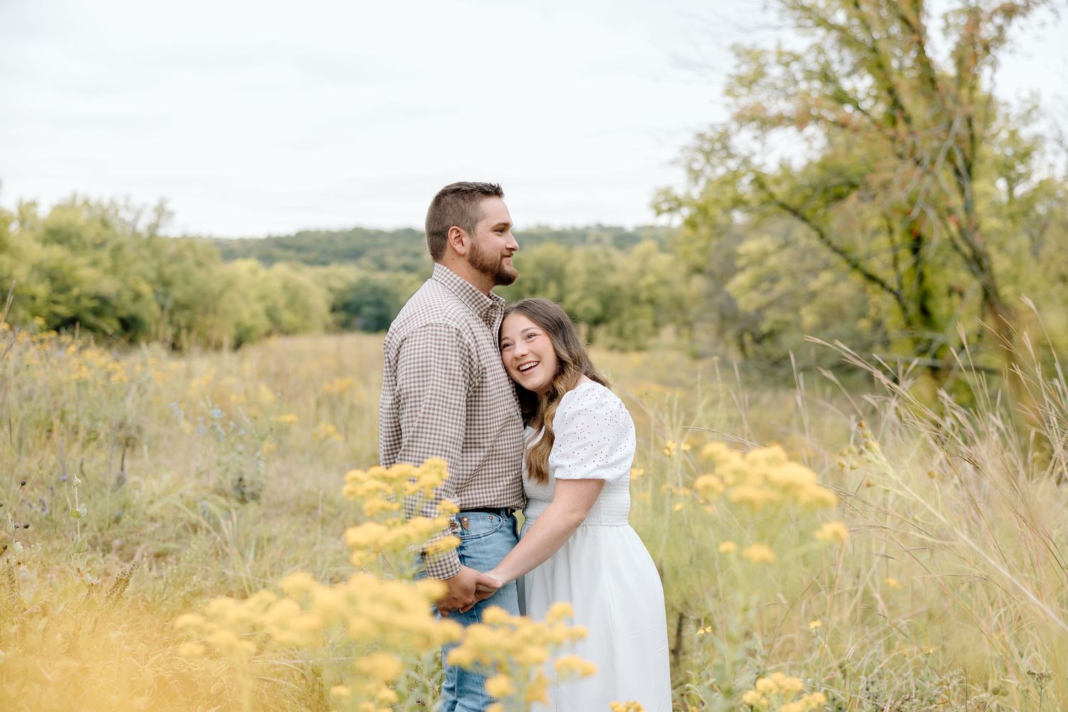 A tender moment between a couple standing in a field of golden flowers with rolling hills in background.