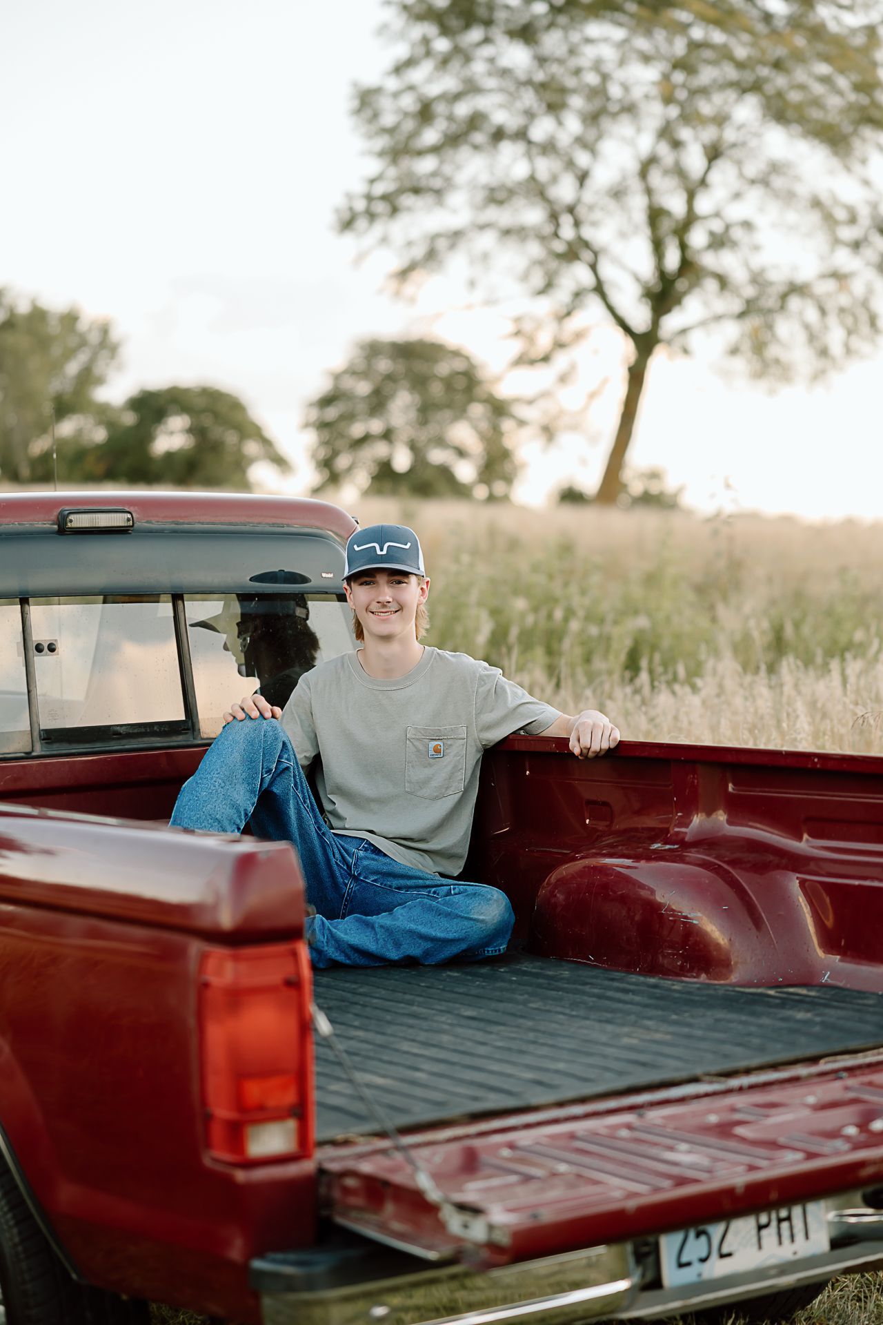 A relaxed pose in the bed of a red pickup truck with a scenic rural backdrop.
