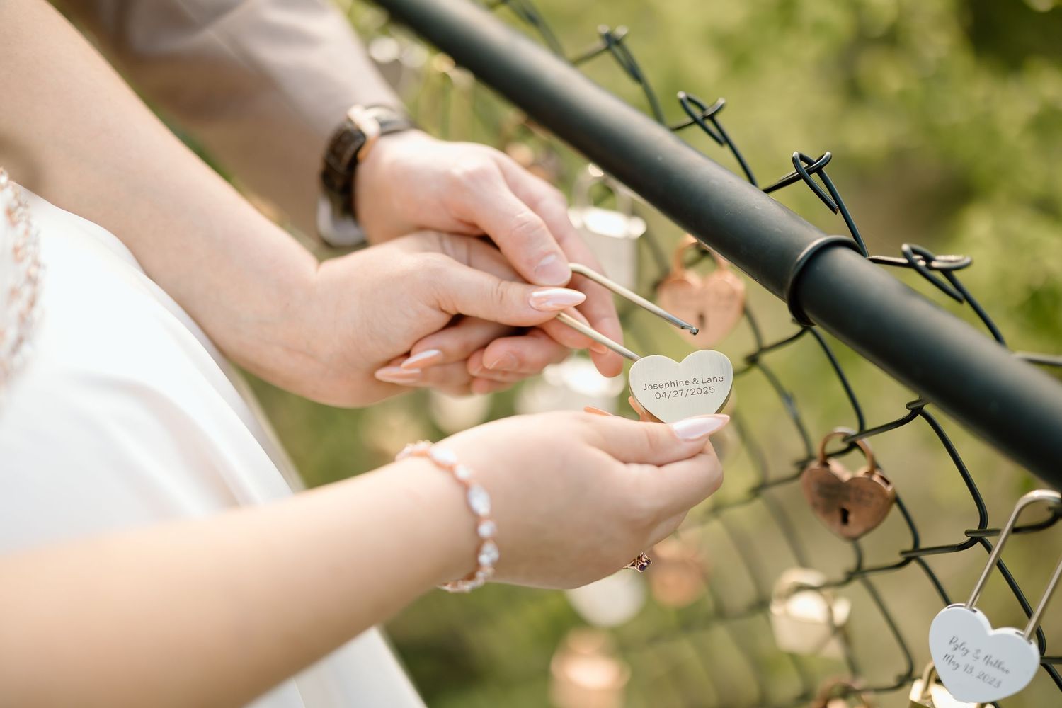 Close-up of hands holding small metallic objects against wire fence.