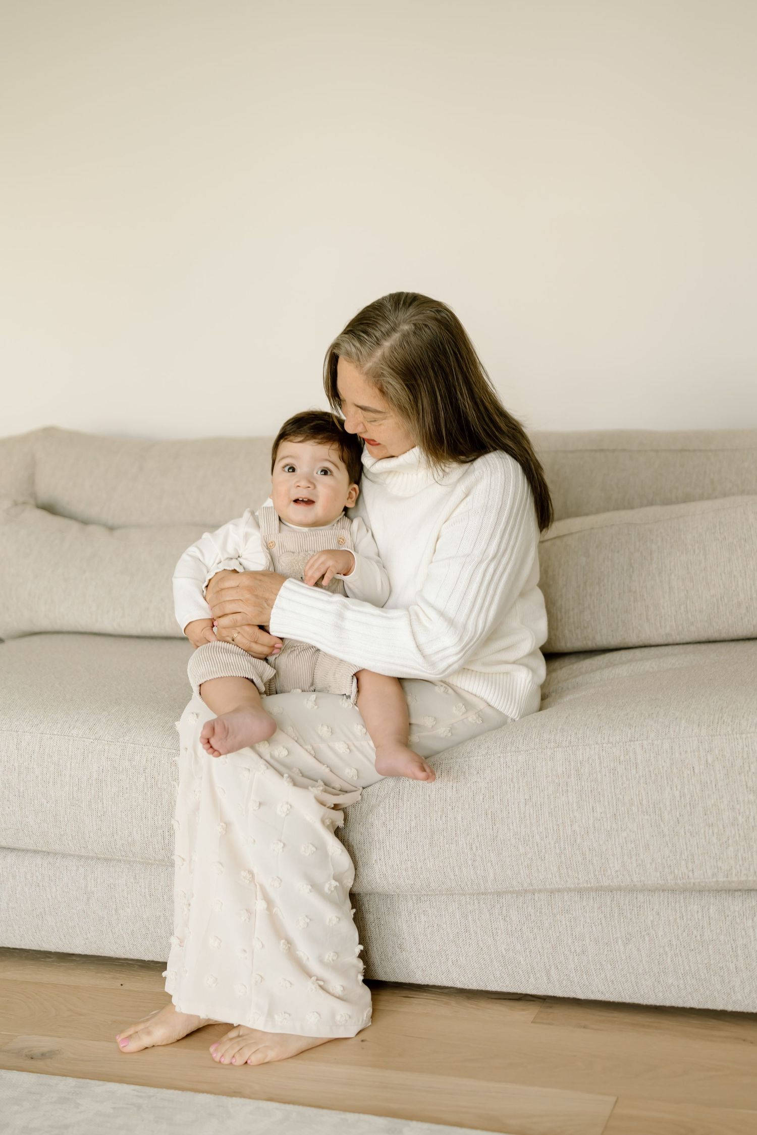 A parent in white sits on a gray couch holding a baby in a white dress, shown in a series of connected photos.