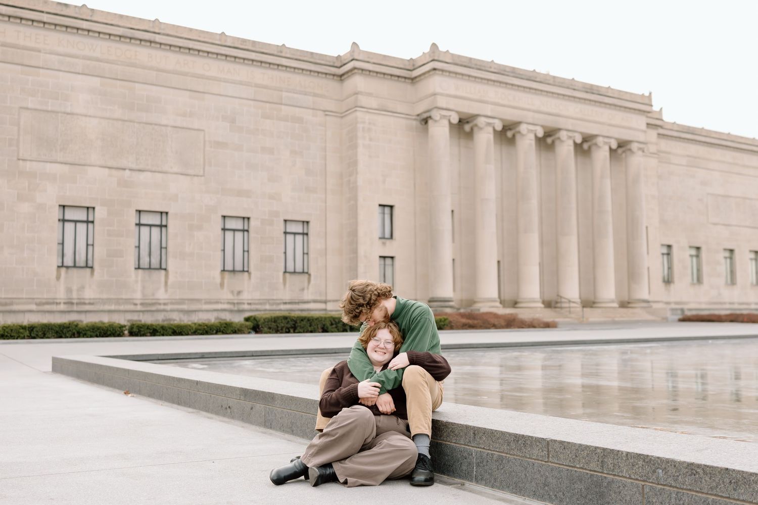 Two people sit together on stone steps outside a grand neoclassical building with columns.