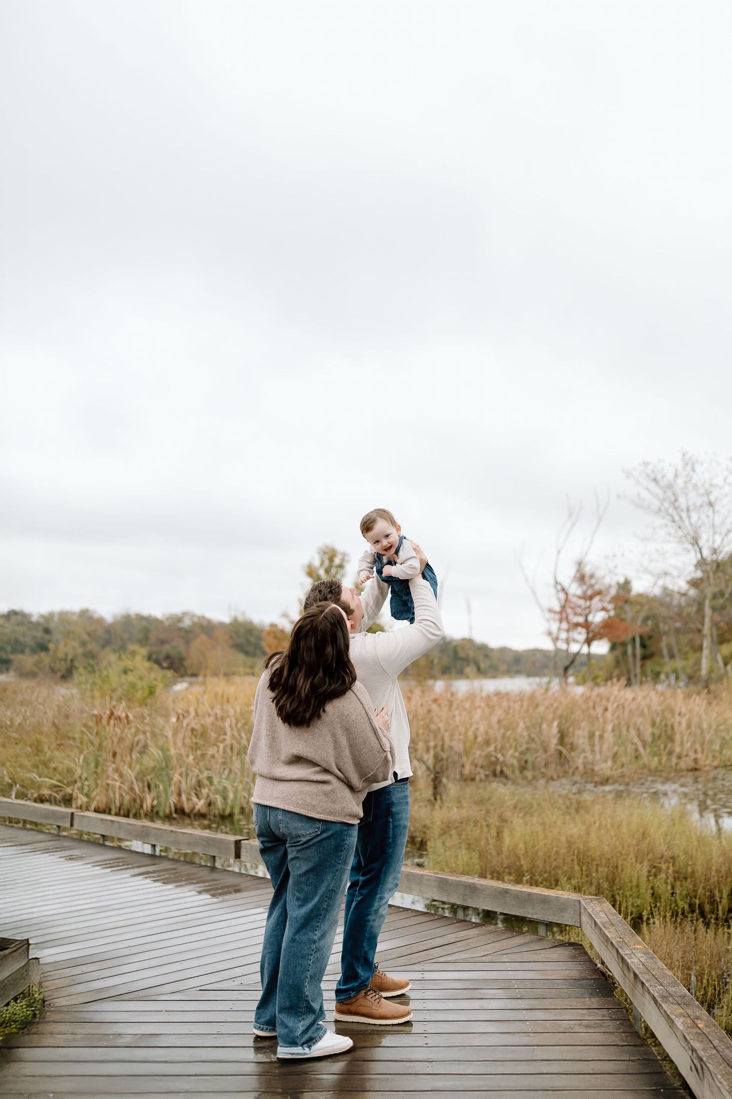 A couple shares a playful moment on a wooden boardwalk surrounded by autumn marsh grass.
