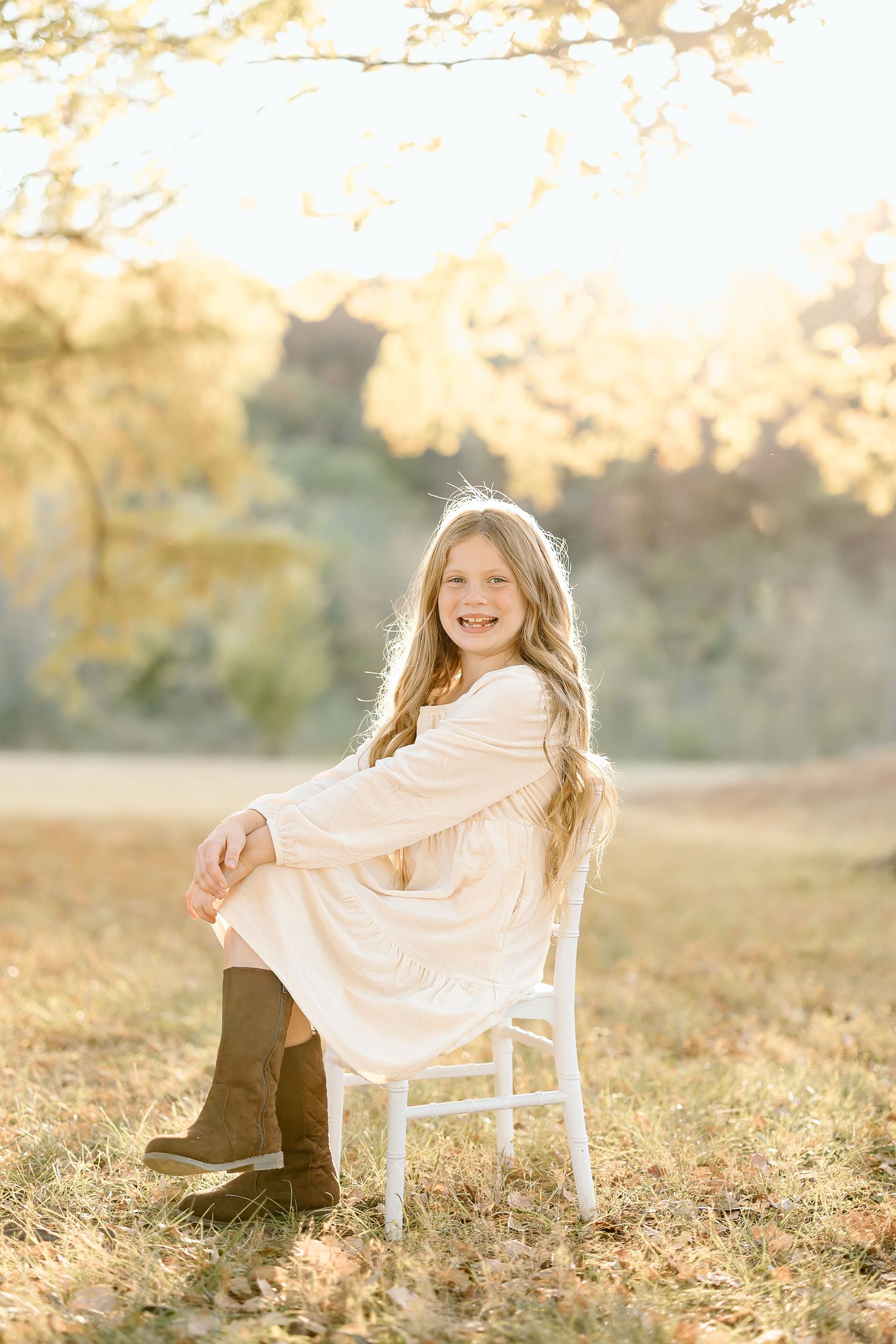 A white chair sits in a sunlit autumn field with fallen leaves during golden hour.