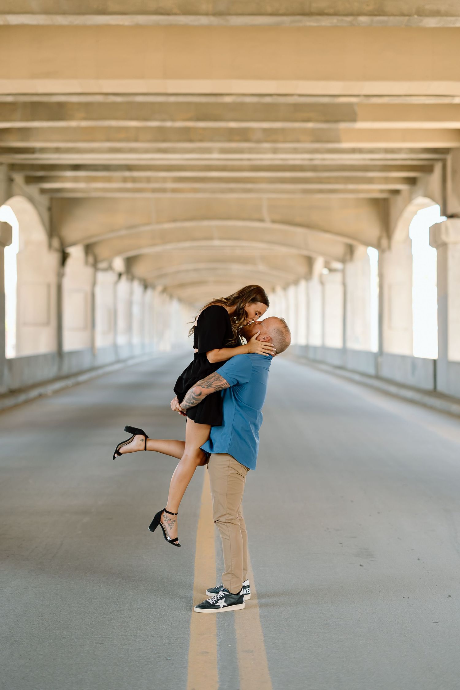 A couple embraces and shares a romantic moment in a covered walkway with repeating architectural columns.