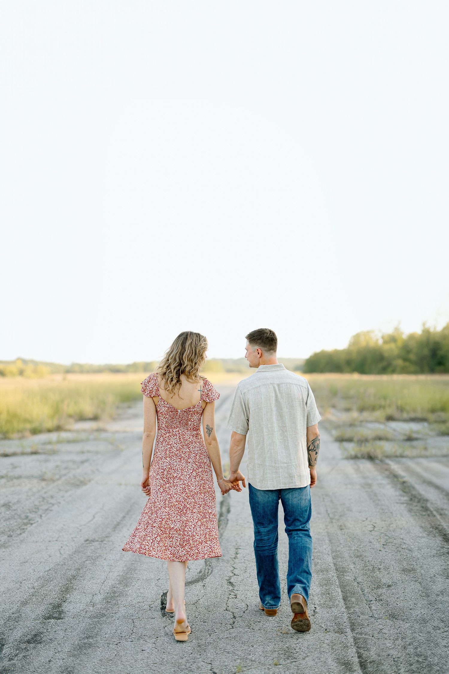 A couple walks hand in hand down a gravel road on a sunny day wearing casual attire.