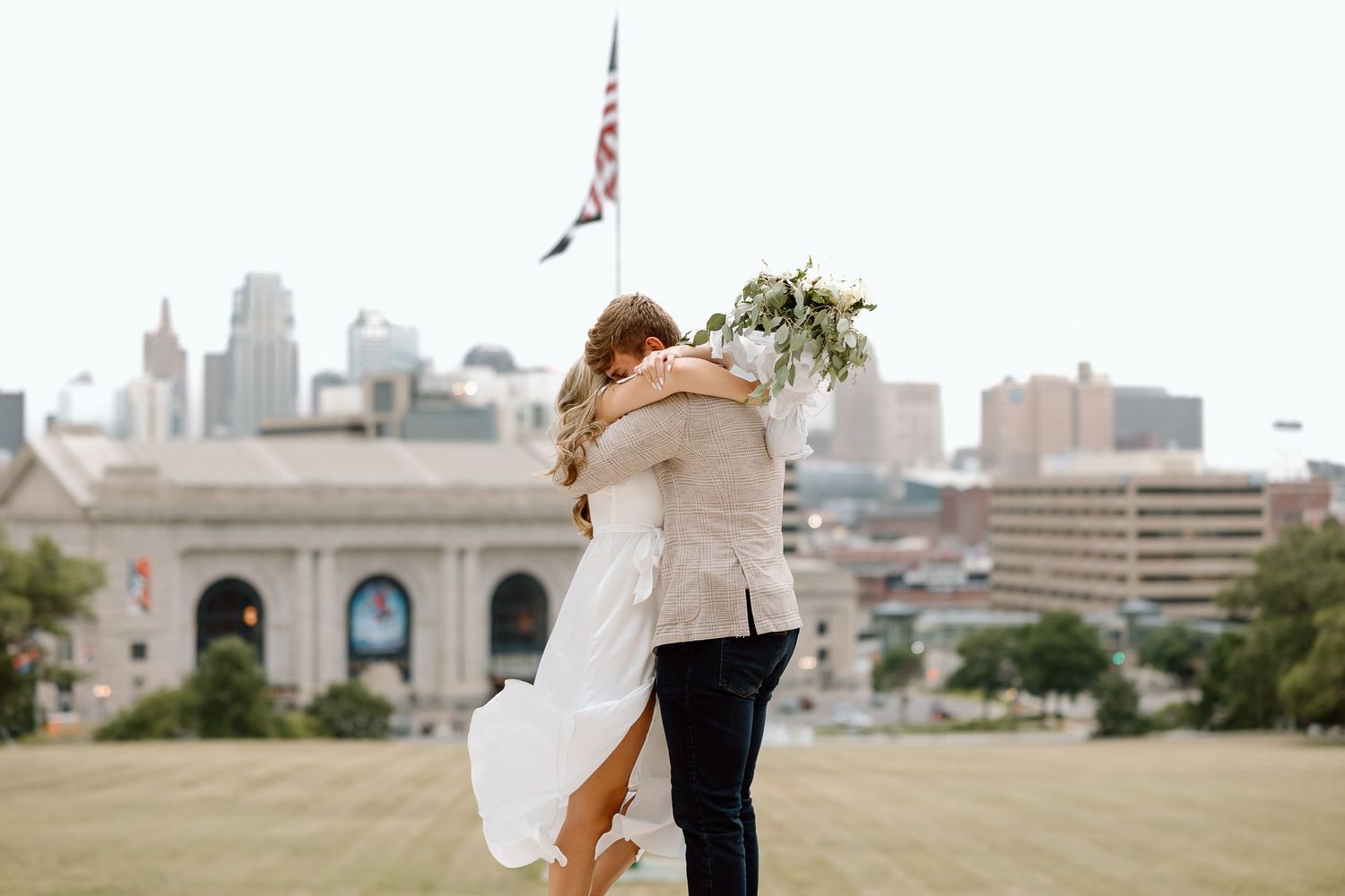 Couple in formal attire dancing together at an outdoor venue with city skyline in the background.