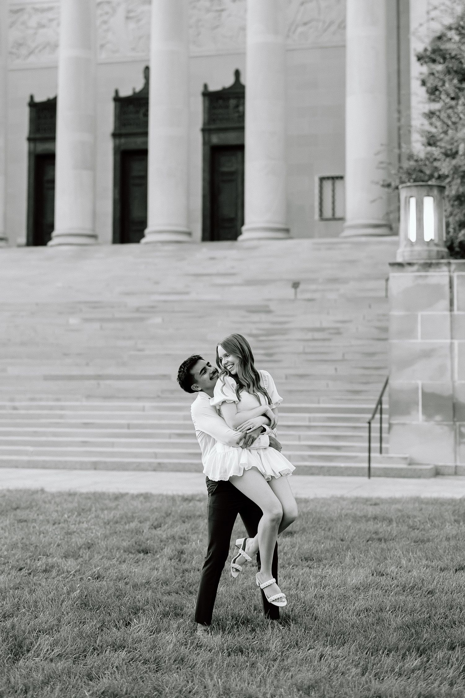 A romantic couple dips in a graceful dance pose on the lawn in front of a grand columned building.