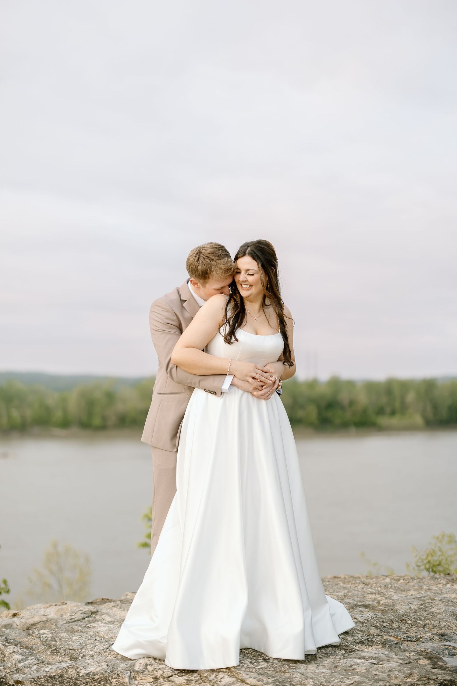 A romantic couple in wedding attire shares tender moments by a lake on overcast day in three sequential photos.