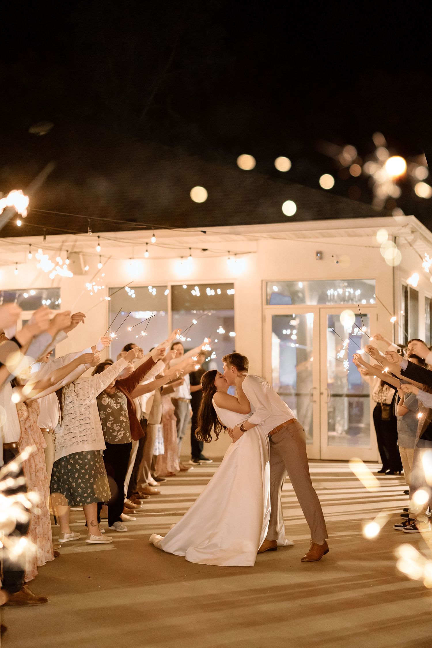 Wedding guests wave sparklers in a line to create a magical nighttime send-off tunnel for the newlyweds.