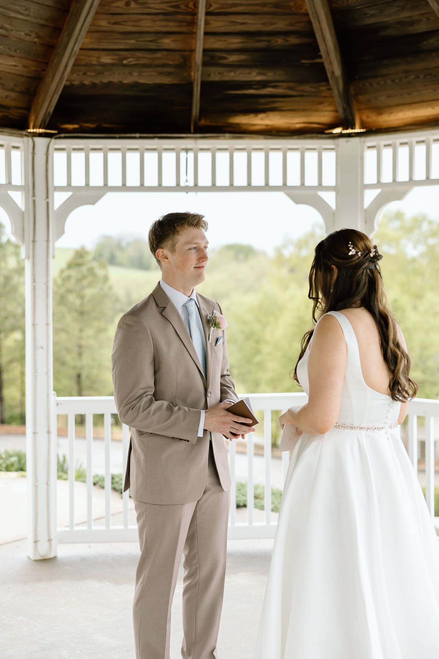 A couple exchanges vows during their wedding ceremony in a white gazebo on a sunny day.