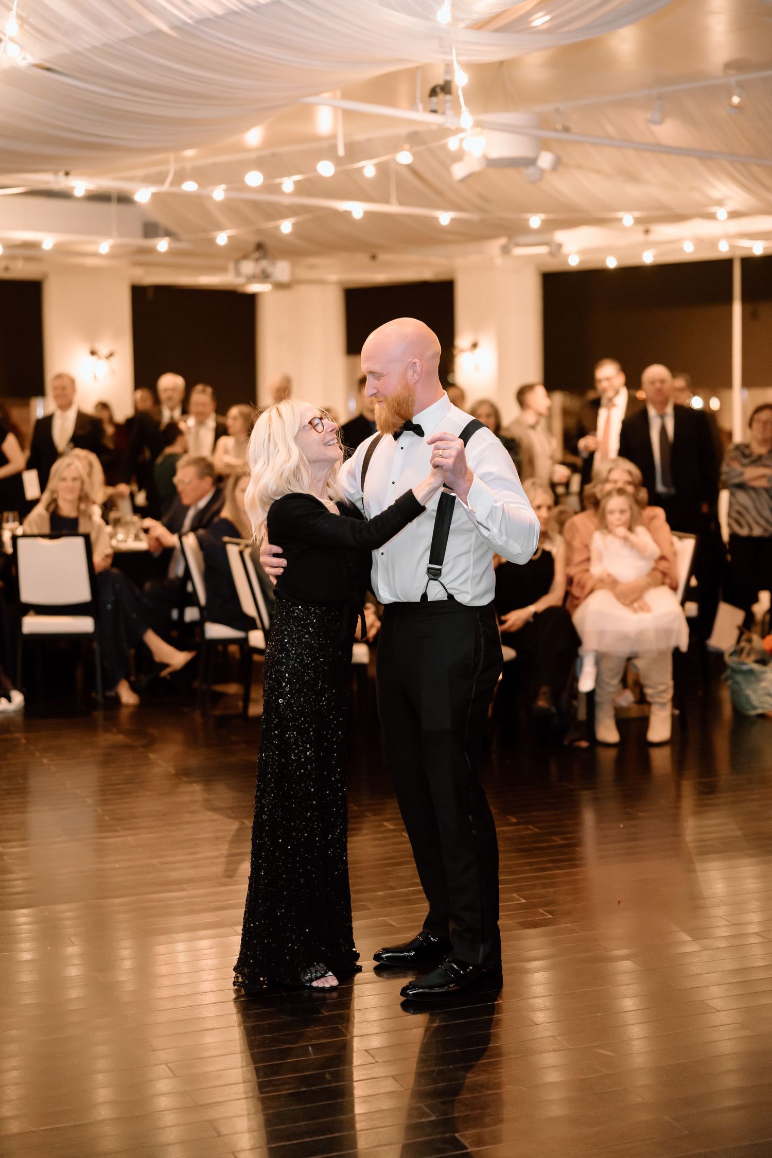 Couples dance together in formal attire at an elegant ballroom event with warm lighting and hardwood floors.