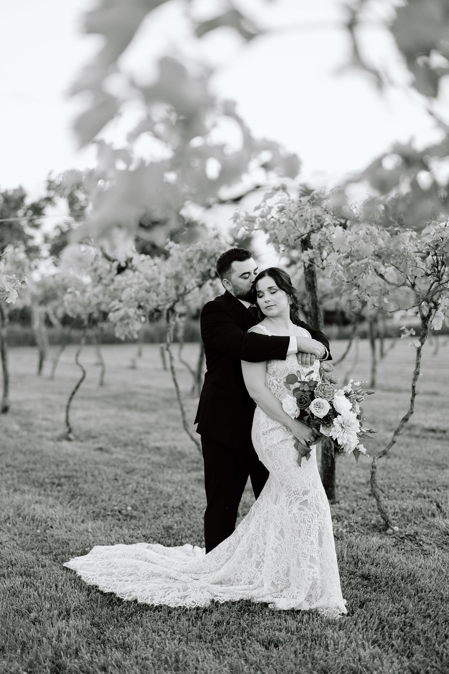 A couple dances together in an orchard setting with the bride wearing a flowing white gown and groom in classic tuxedo.