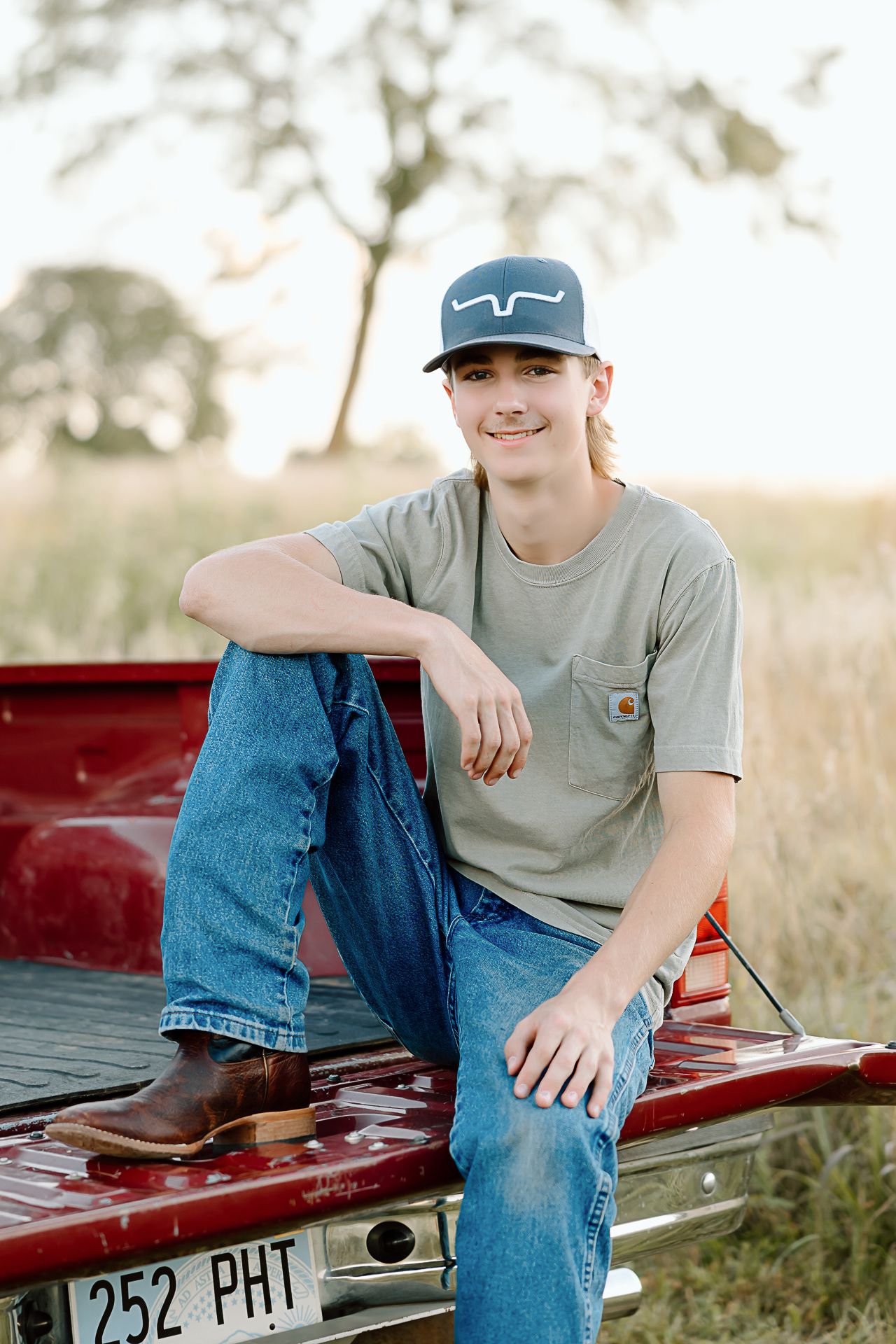 Portrait shot of someone wearing a baseball cap and gray t-shirt sitting on a red pickup truck bed.