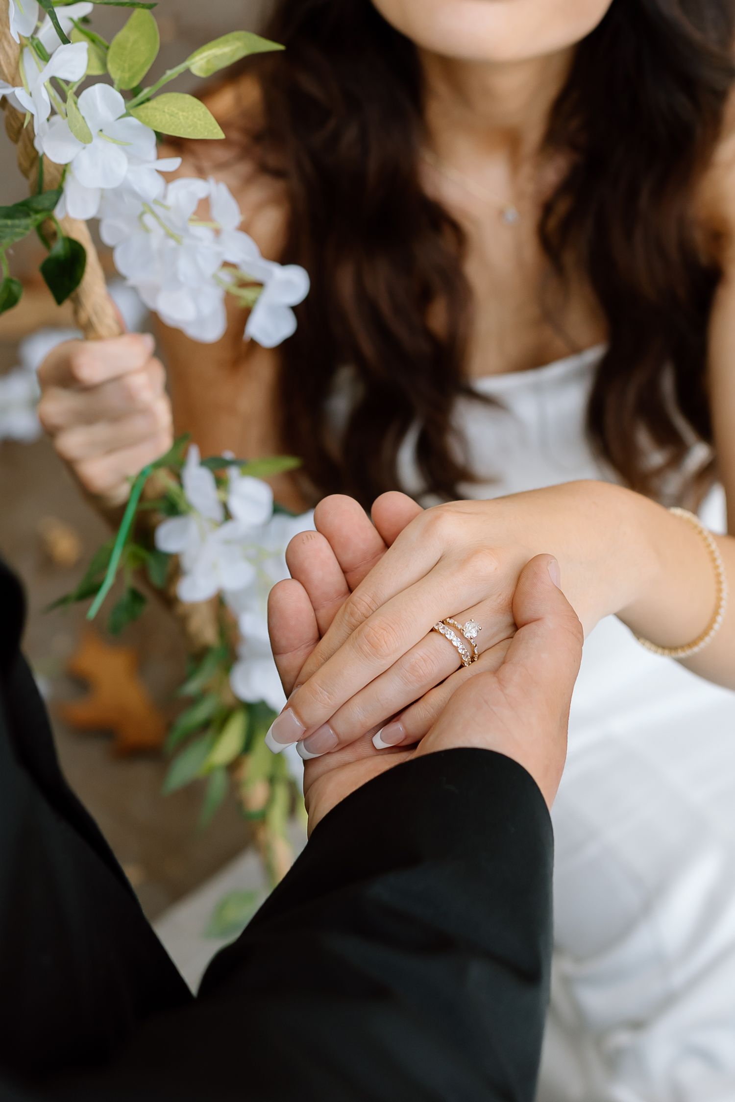 Close-up shots of hands wearing engagement ring with white flowers and greenery in the background.