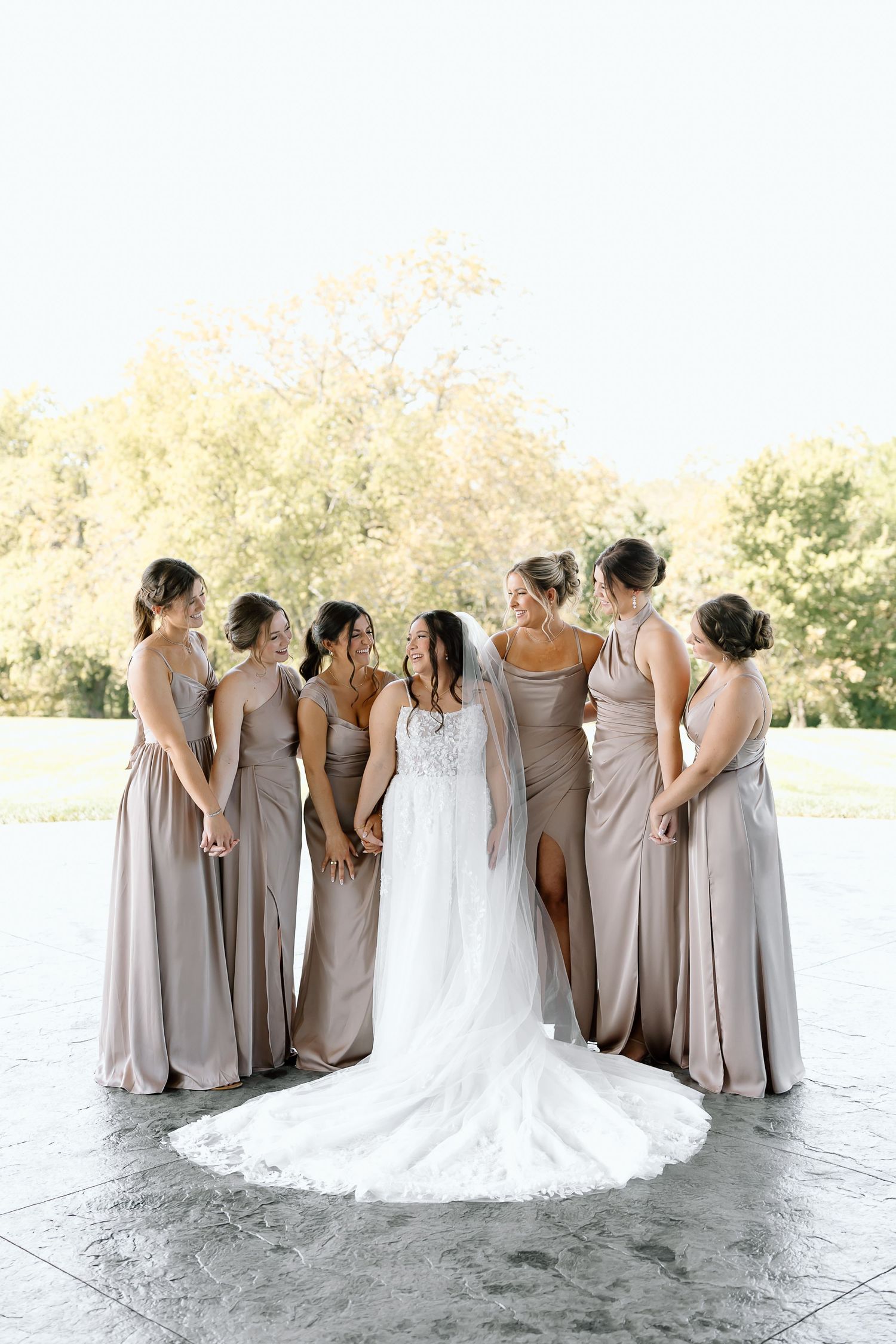 A bridal party in matching gray dresses poses together on a patio during an elegant outdoor wedding celebration.