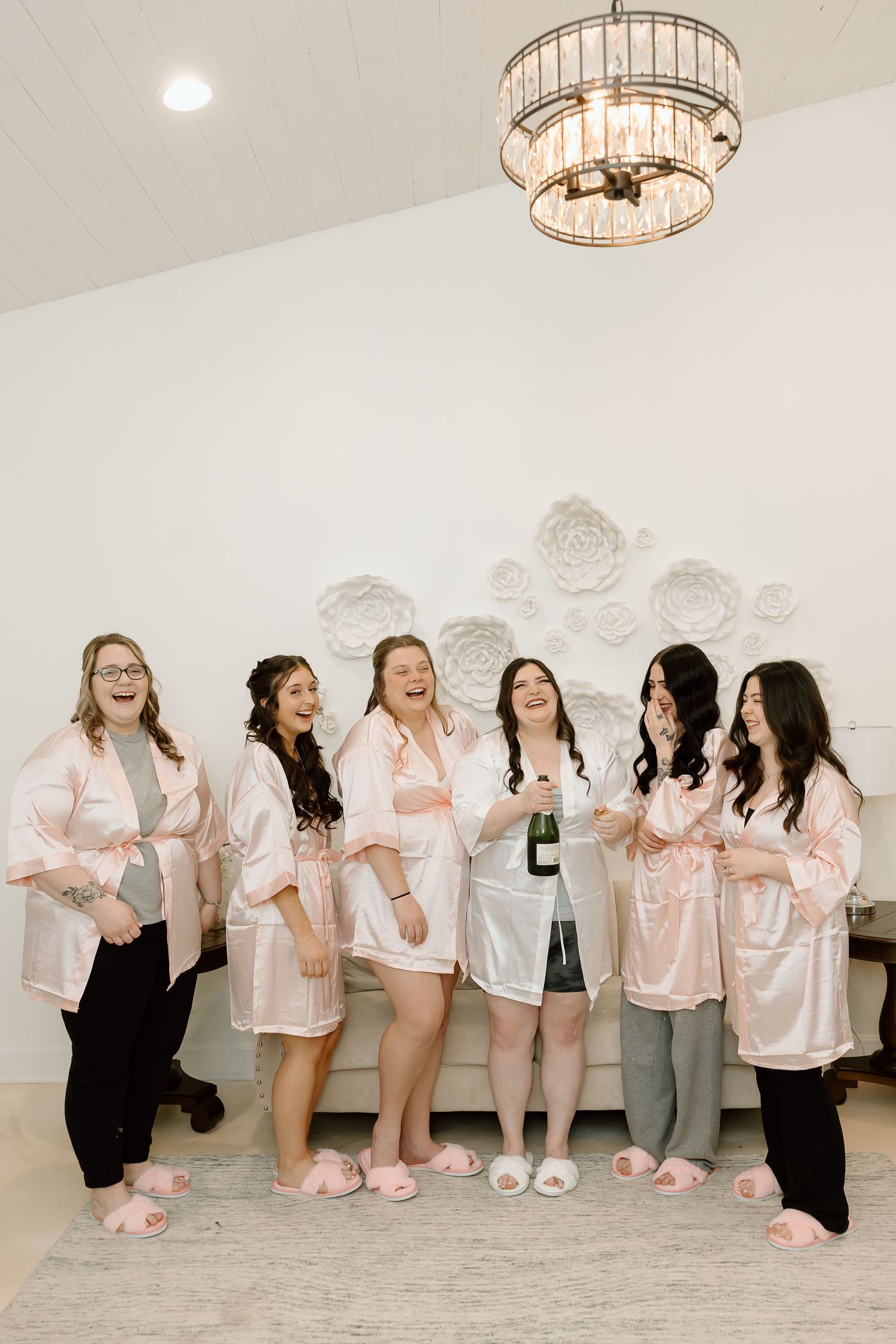A group wearing matching pink satin robes and slippers poses together for candid photos in a white room.