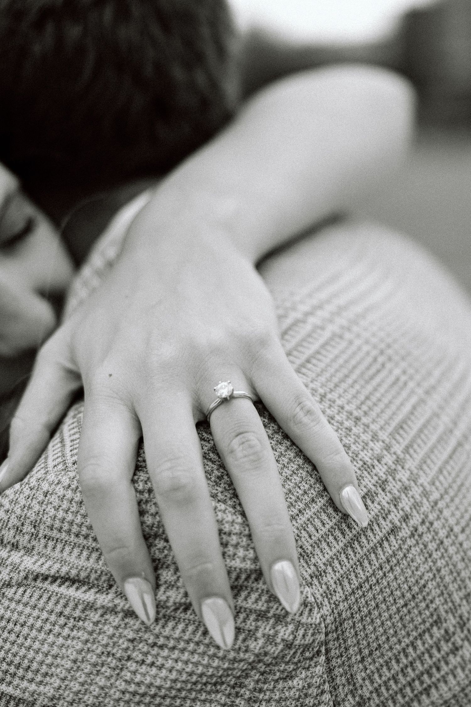 Close-up view of a hand with long manicured nails resting on a textured gray knit fabric surface.