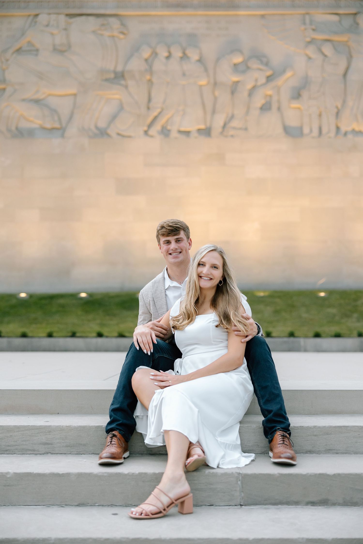 A couple sits together on concrete steps wearing casual attire during an outdoor photo session.