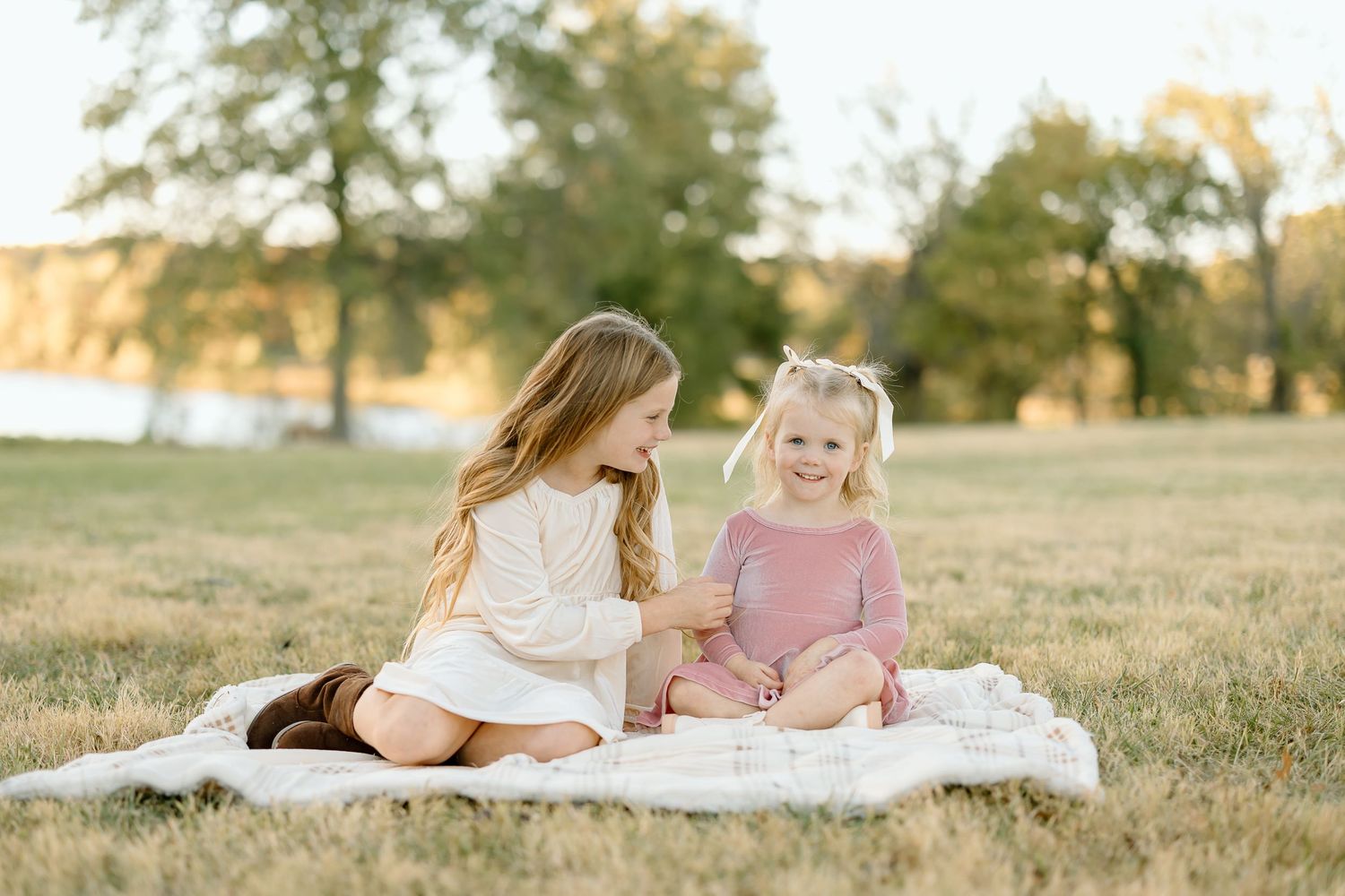 Two people sit together on grass during golden hour at sunset in a field.