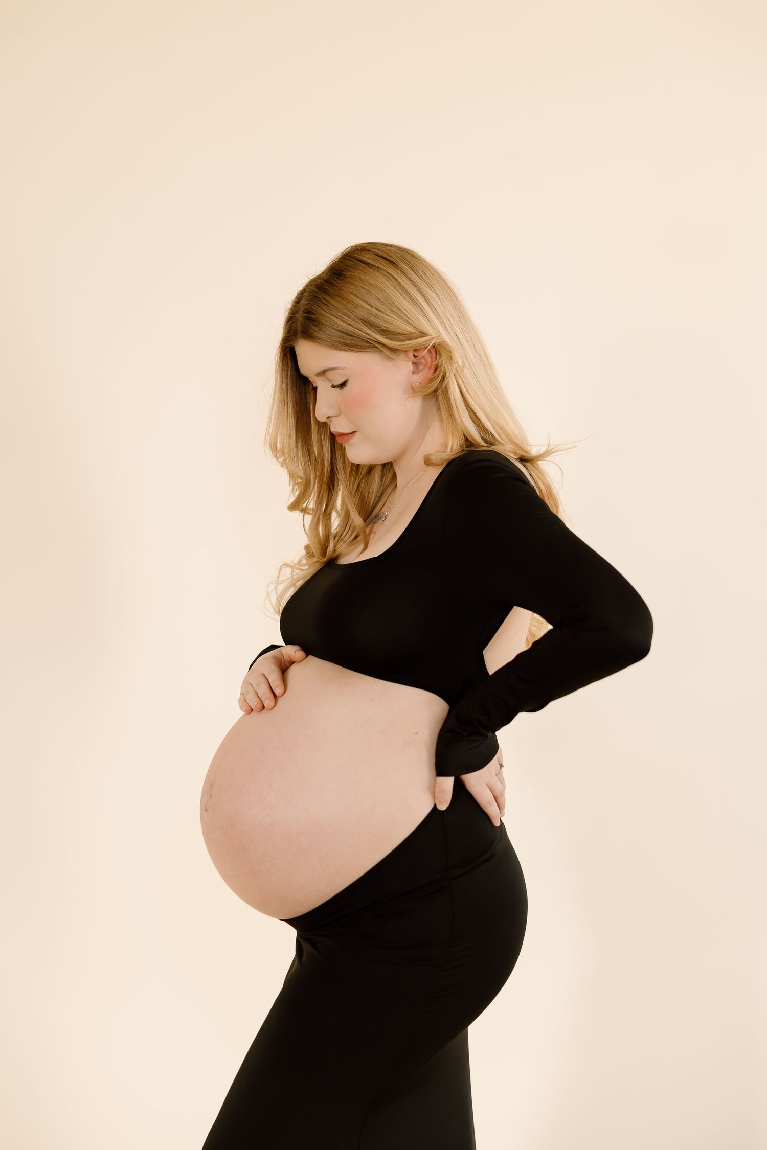 Three artistic maternity photos of a pregnant woman in black against beige background showing her growing belly.