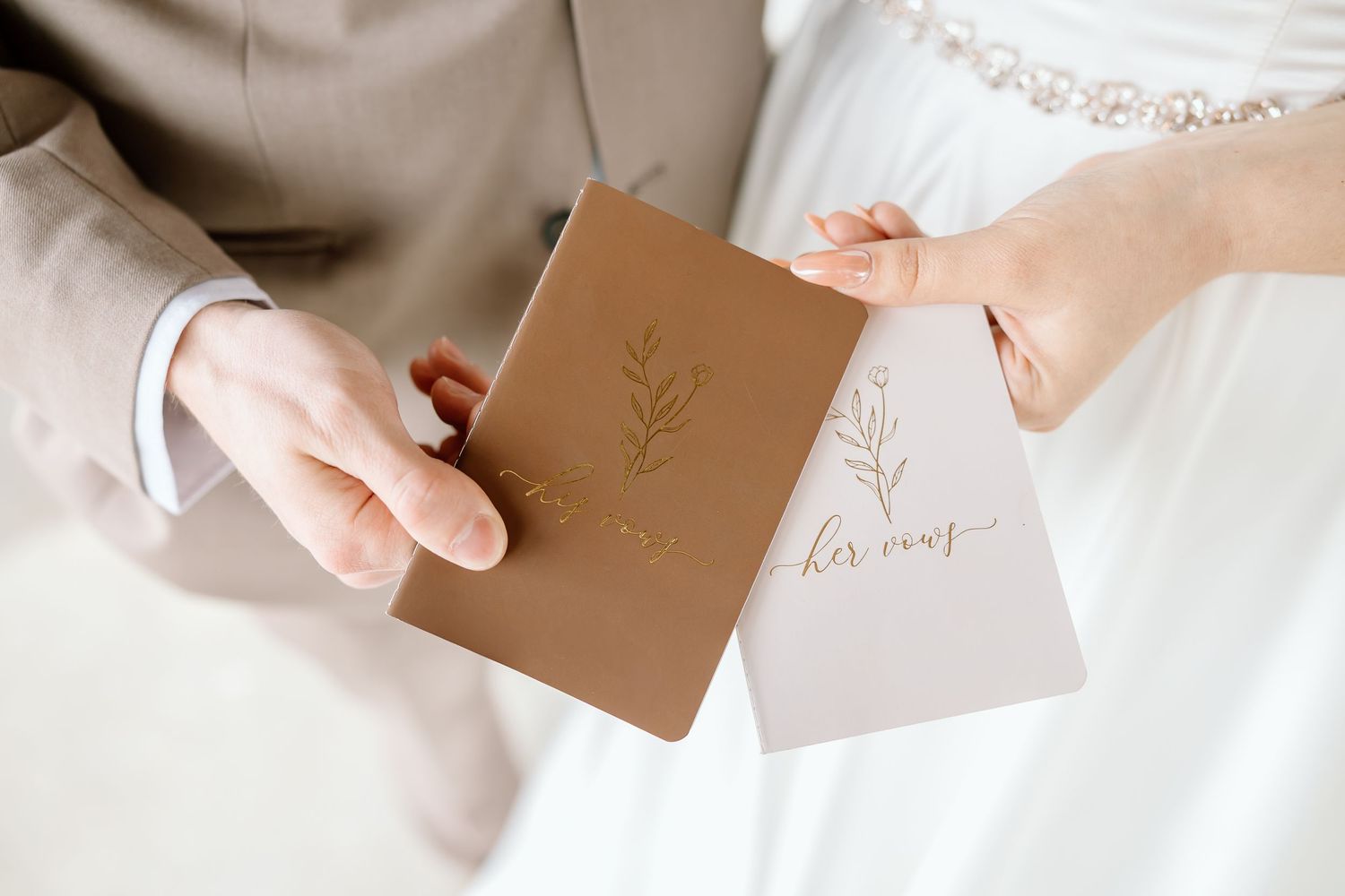 Hands holding minimal brown kraft paper cards with elegant gold calligraphy writing against white background.
