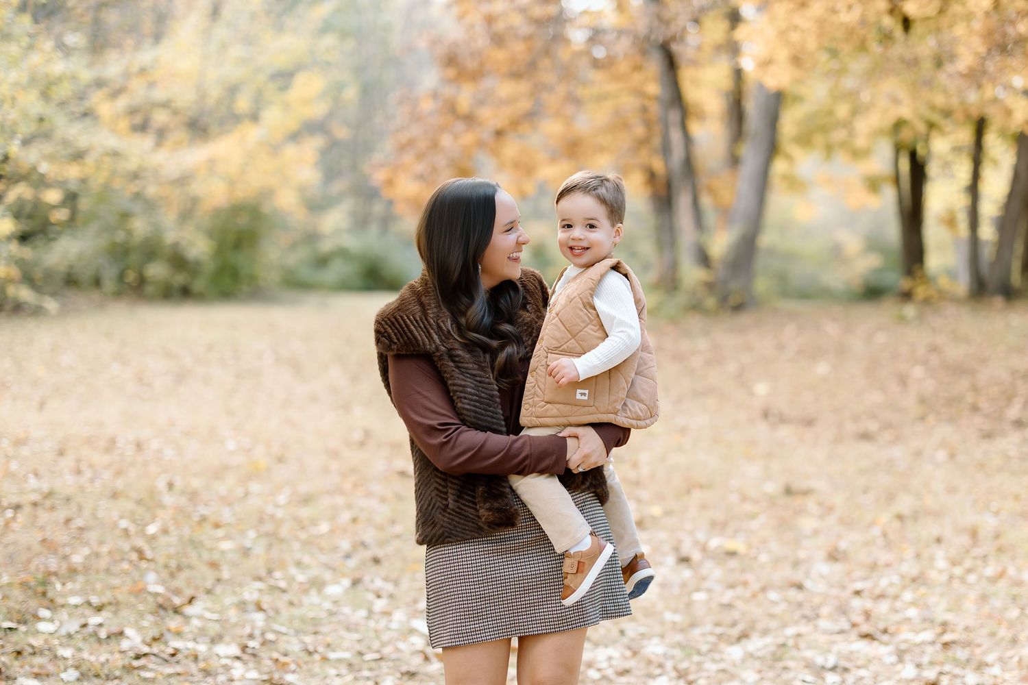 A family plays together in a park during autumn as colorful fallen leaves cover the ground.