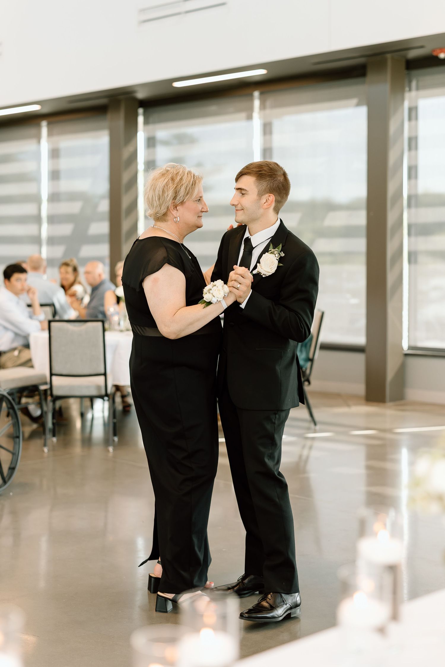 A couple dances together in an elegant ballroom dance, sharing a tender moment in a bright, spacious room.