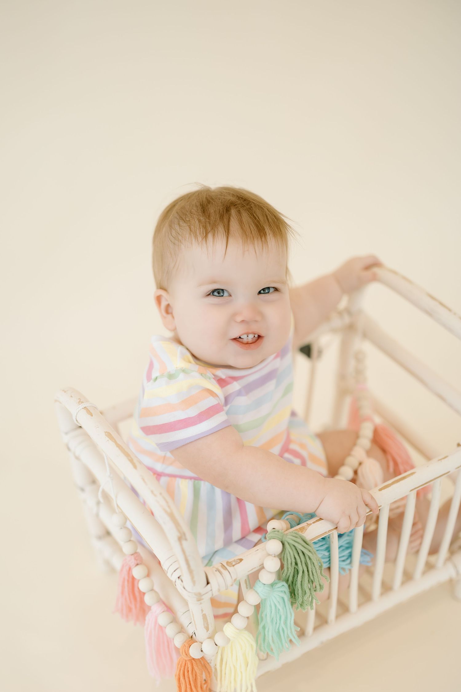 A baby in a white crib plays with colorful tassels hanging from the railing in a series of candid shots.