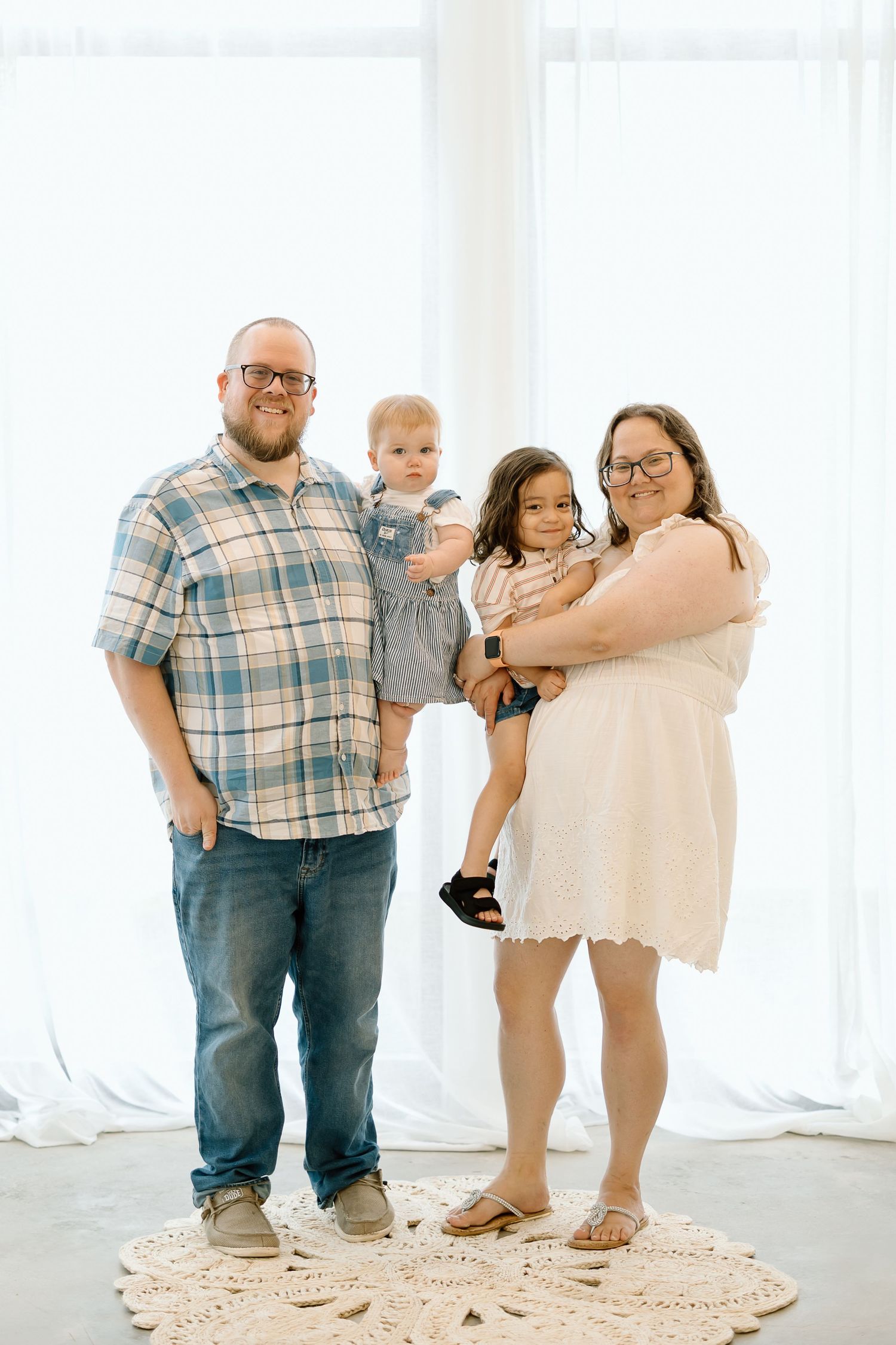 Family portrait on a round rug in a bright white room with casual attire and warm smiles.