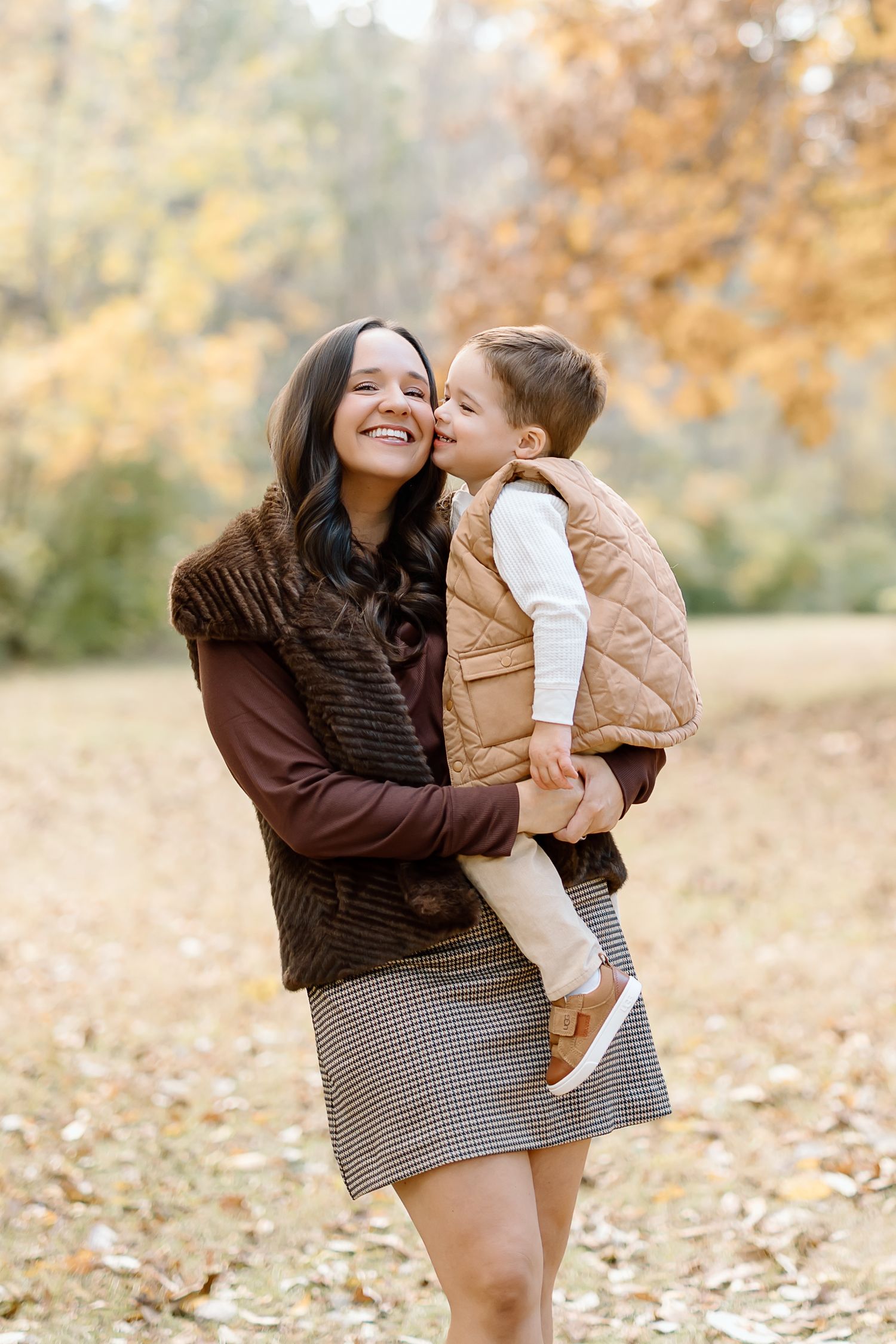 A parent and child share joyful moments together outdoors during autumn with fallen leaves in the background.