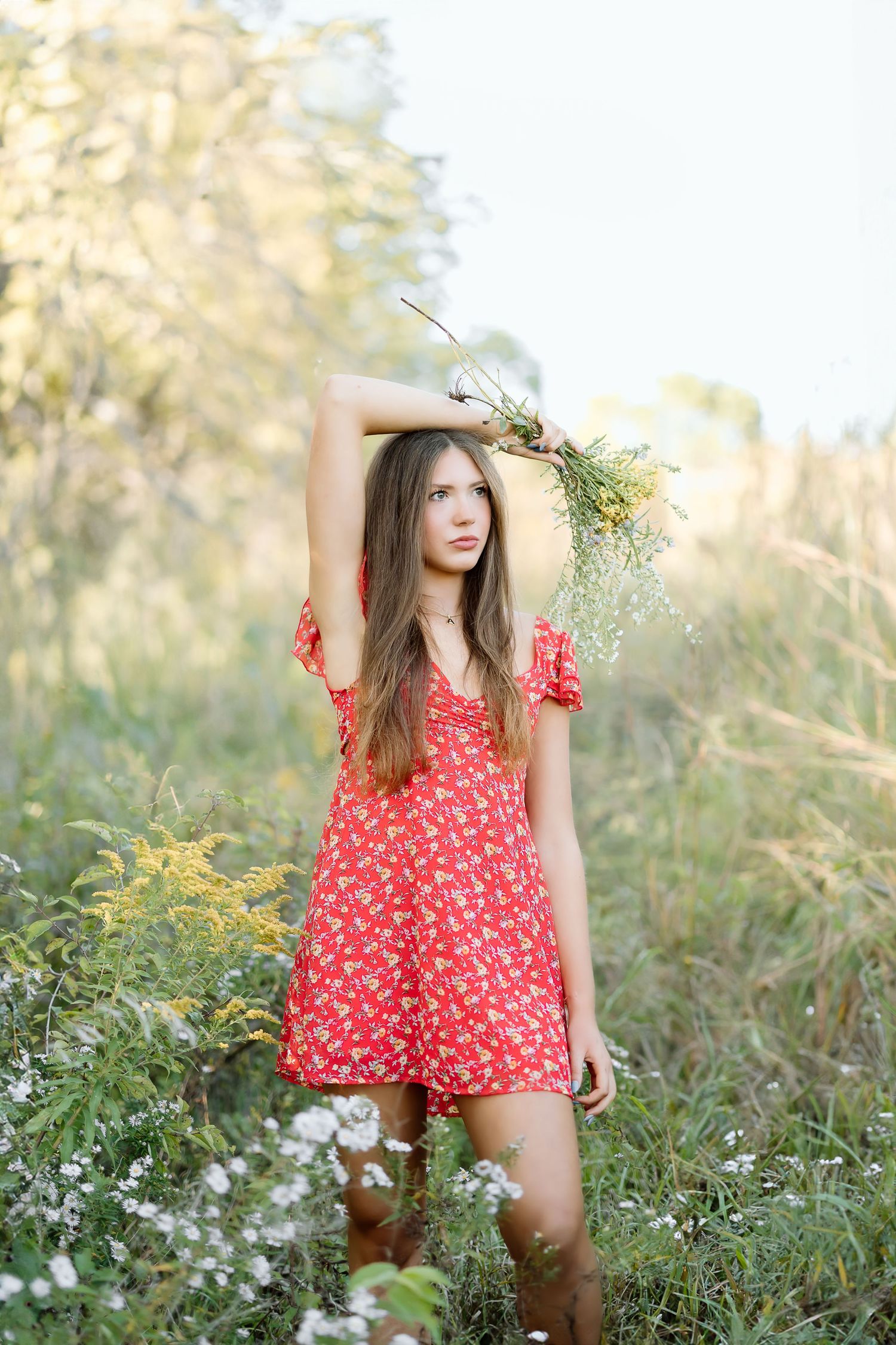 A person in a red floral romper poses gracefully among wildflowers in a sunlit meadow during golden hour.