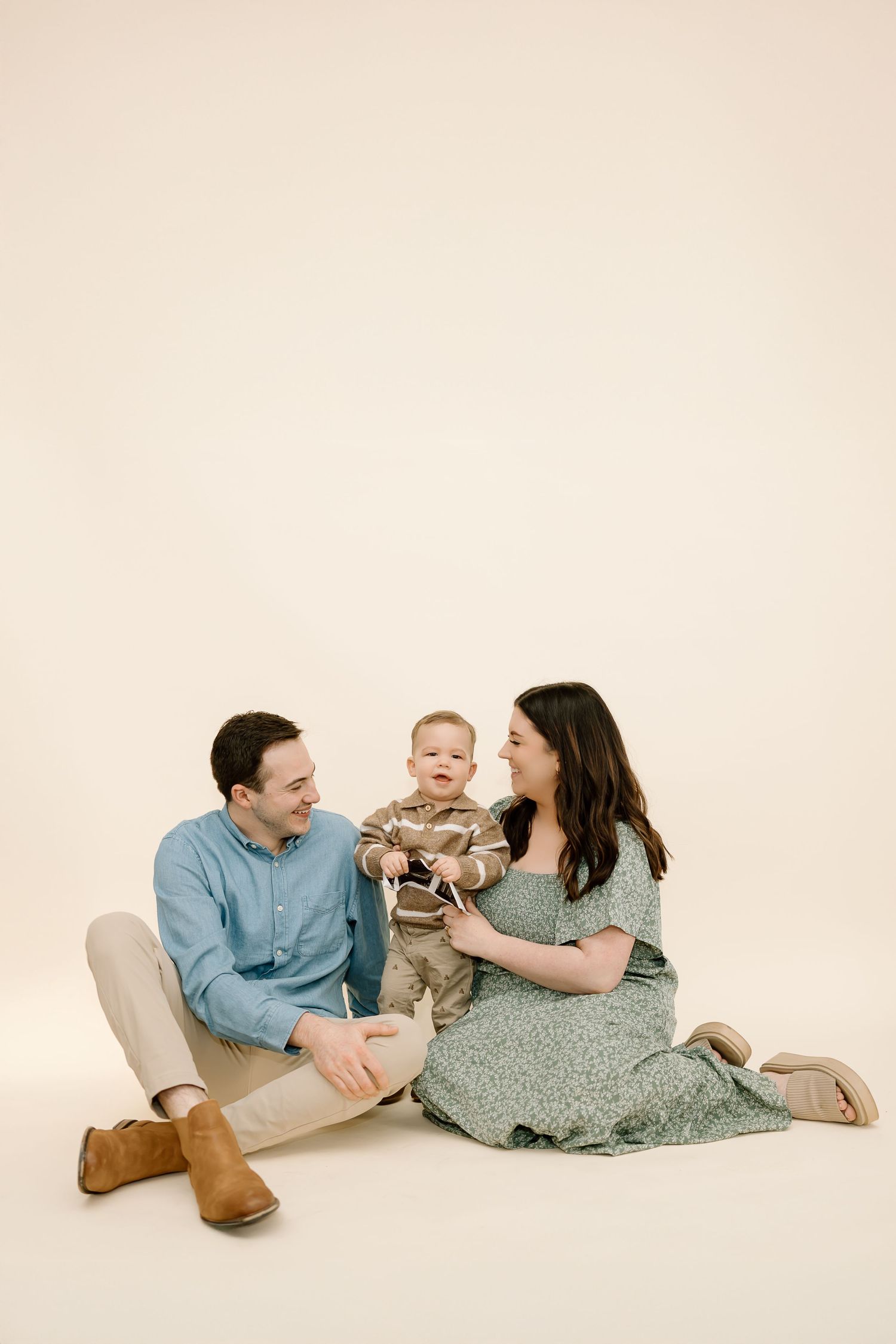Family of three in casual attire laying on cream colored floor sharing playful moments together.