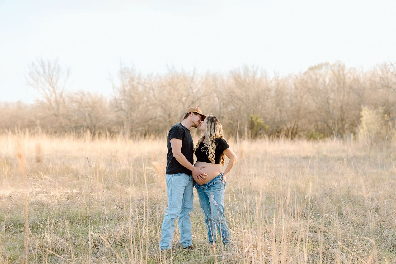 Couple standing together in tall golden grass during sunset in a rural field.