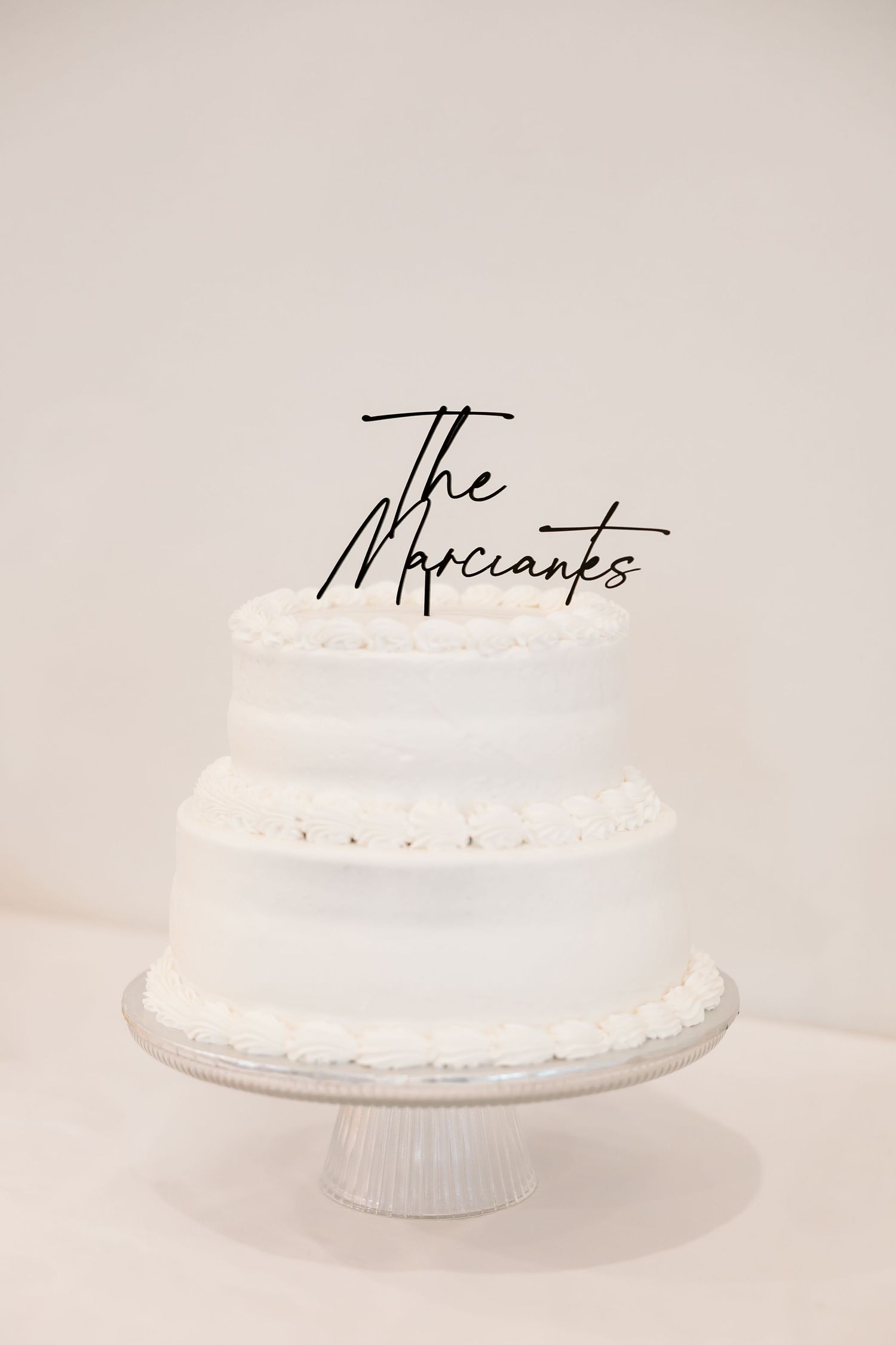 A white wedding cake displayed on a classic pedestal cake stand against a light background.