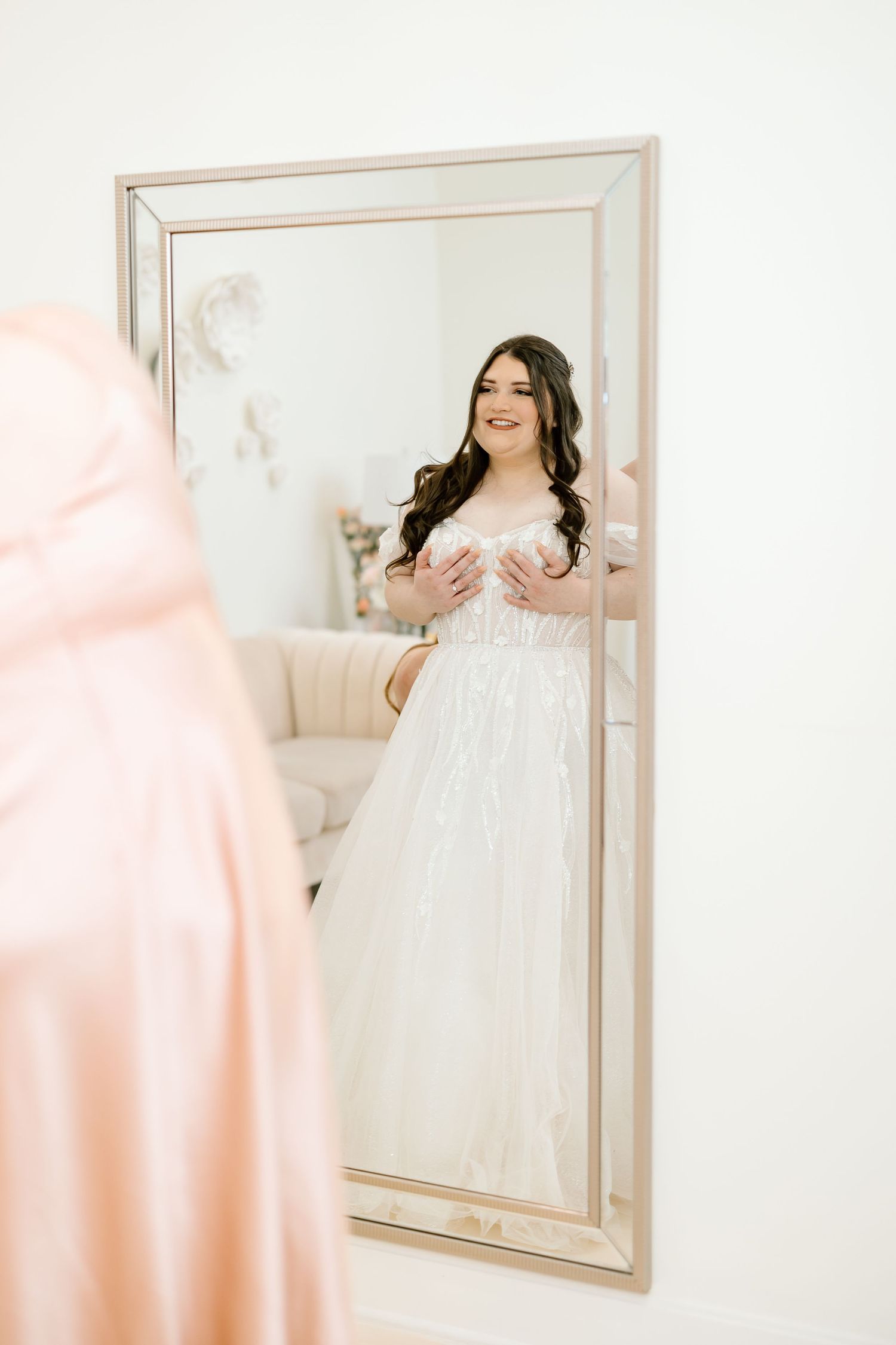 Mirror reflection shows a white lace wedding dress with long sleeves in an elegant bridal suite interior.