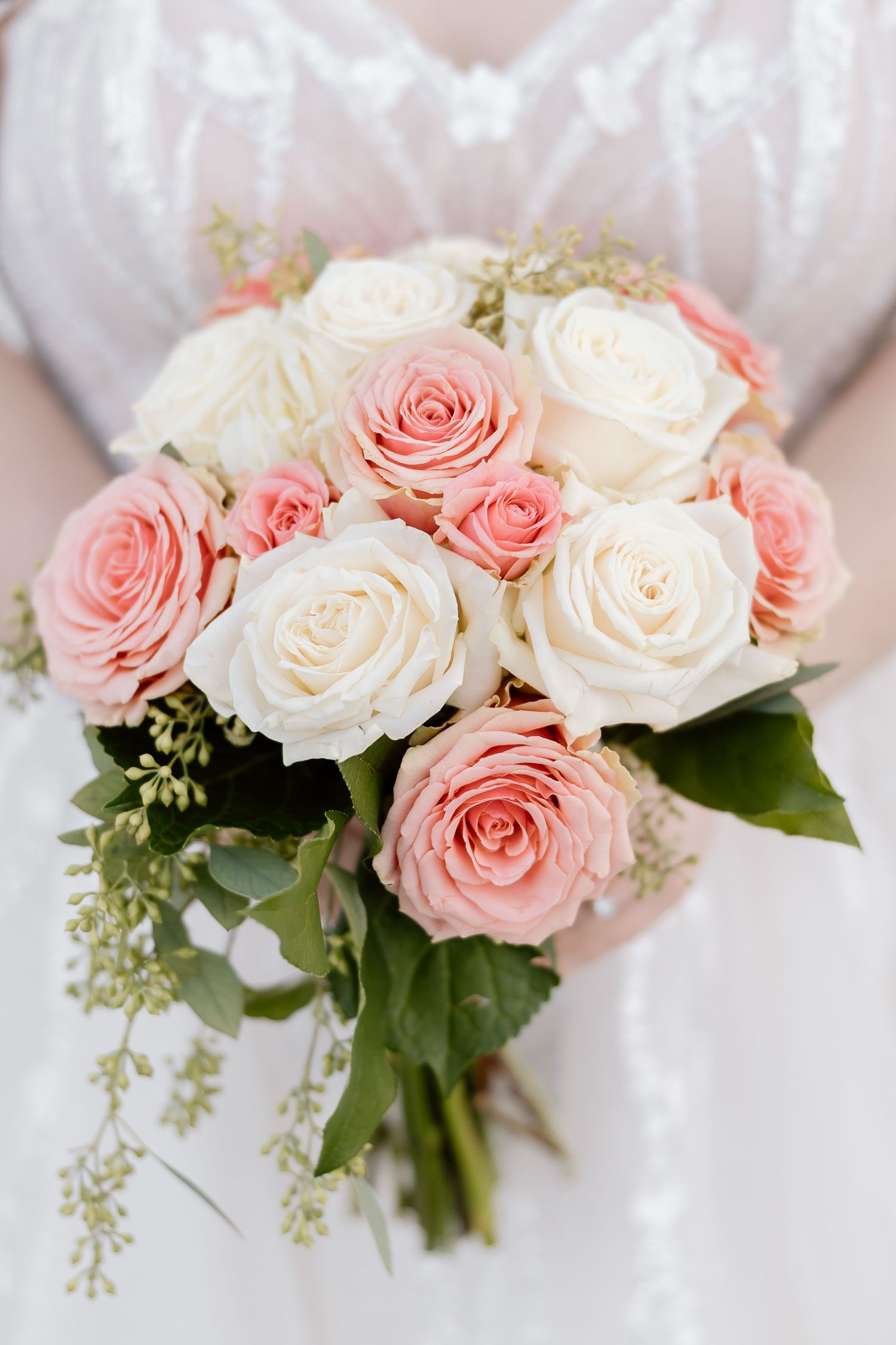 Elegant bouquet of pink and white roses with delicate greenery against a soft white background.