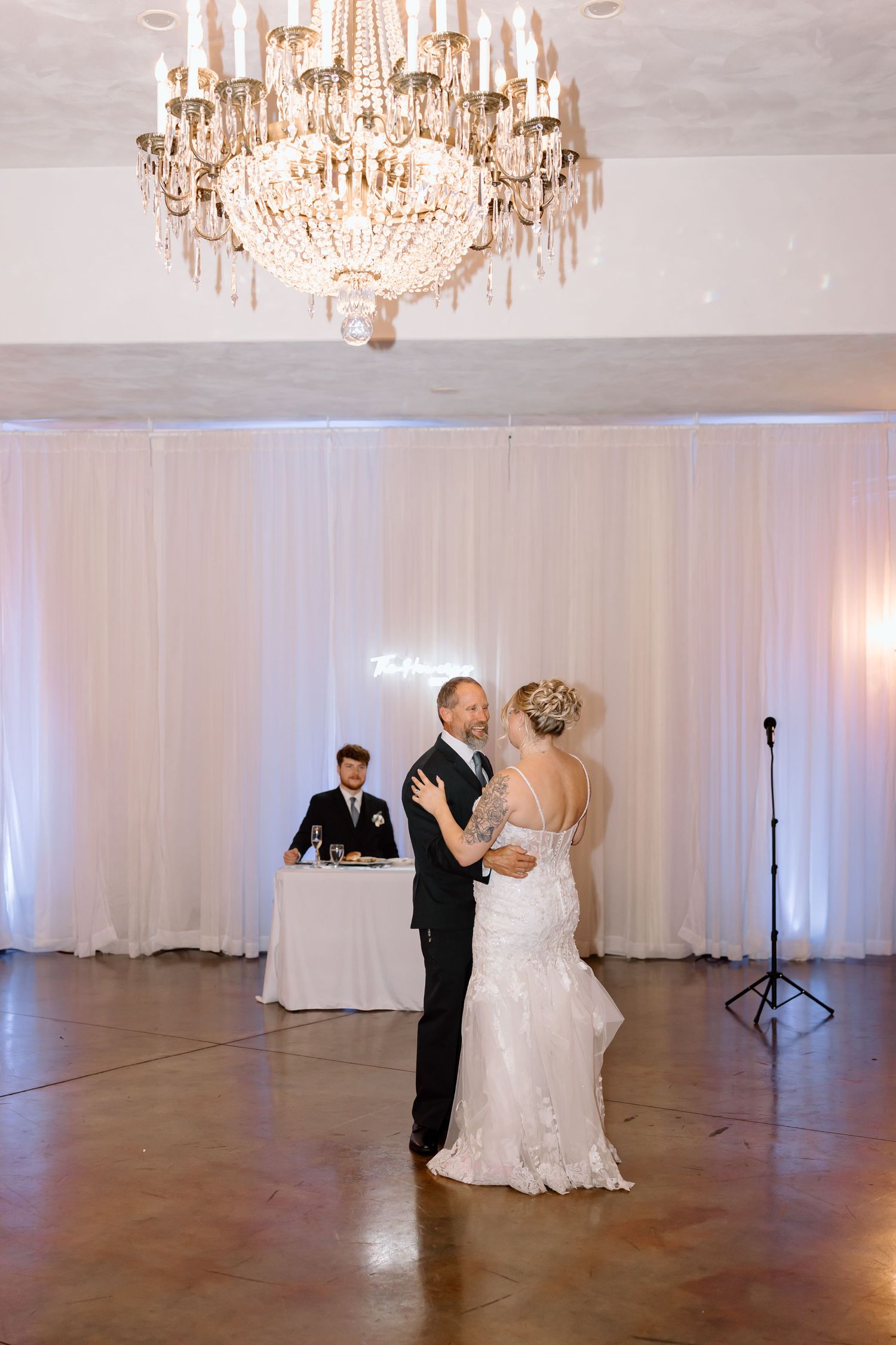 Wedding celebration in a luxurious venue featuring crystal chandeliers and couples dancing on a polished floor.