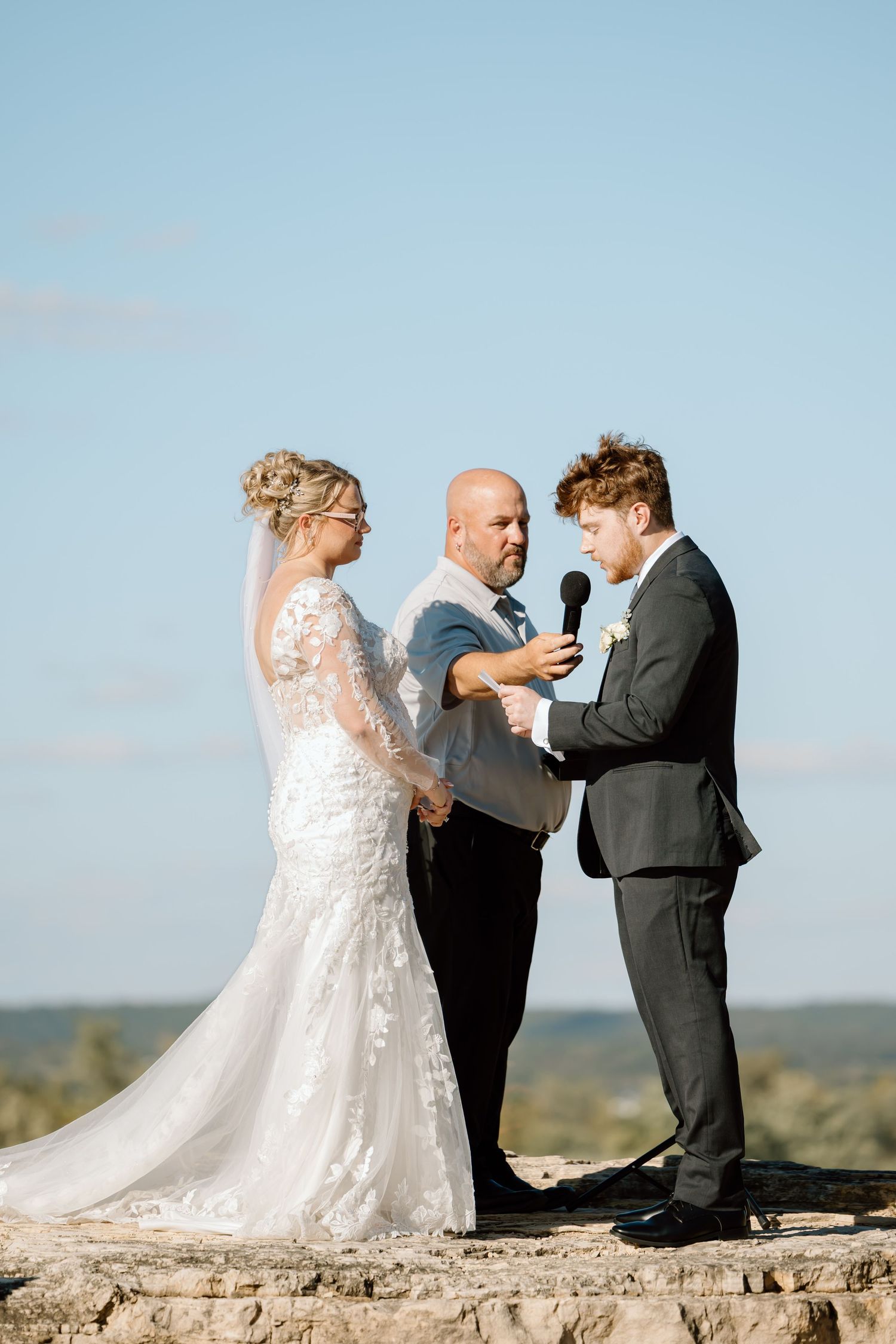 Wedding ceremony takes place outdoors on a scenic cliff with beautiful sky in the background.
